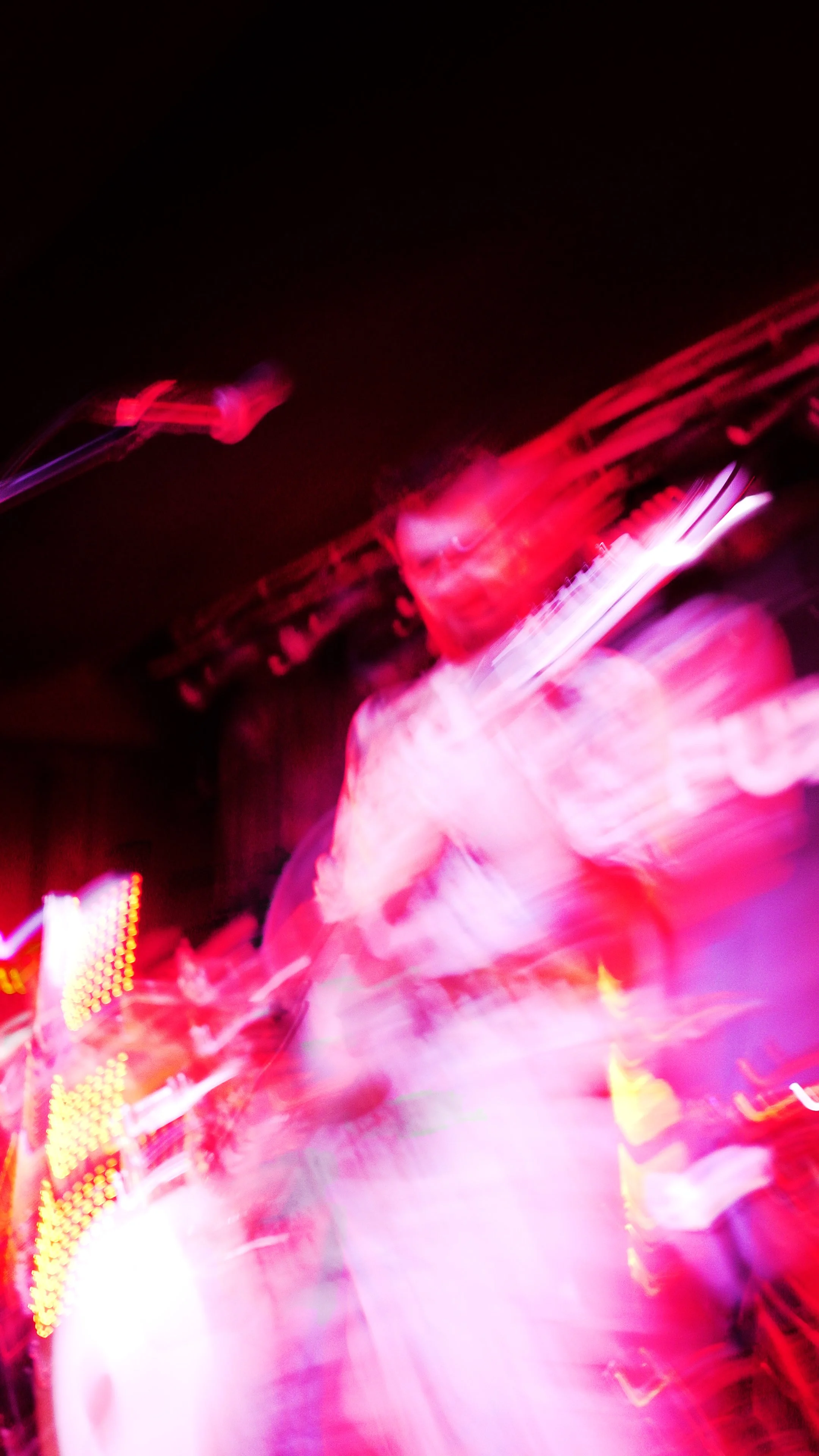 Blurry image of a person playing a guitar on stage with pink and purple lighting effects.
