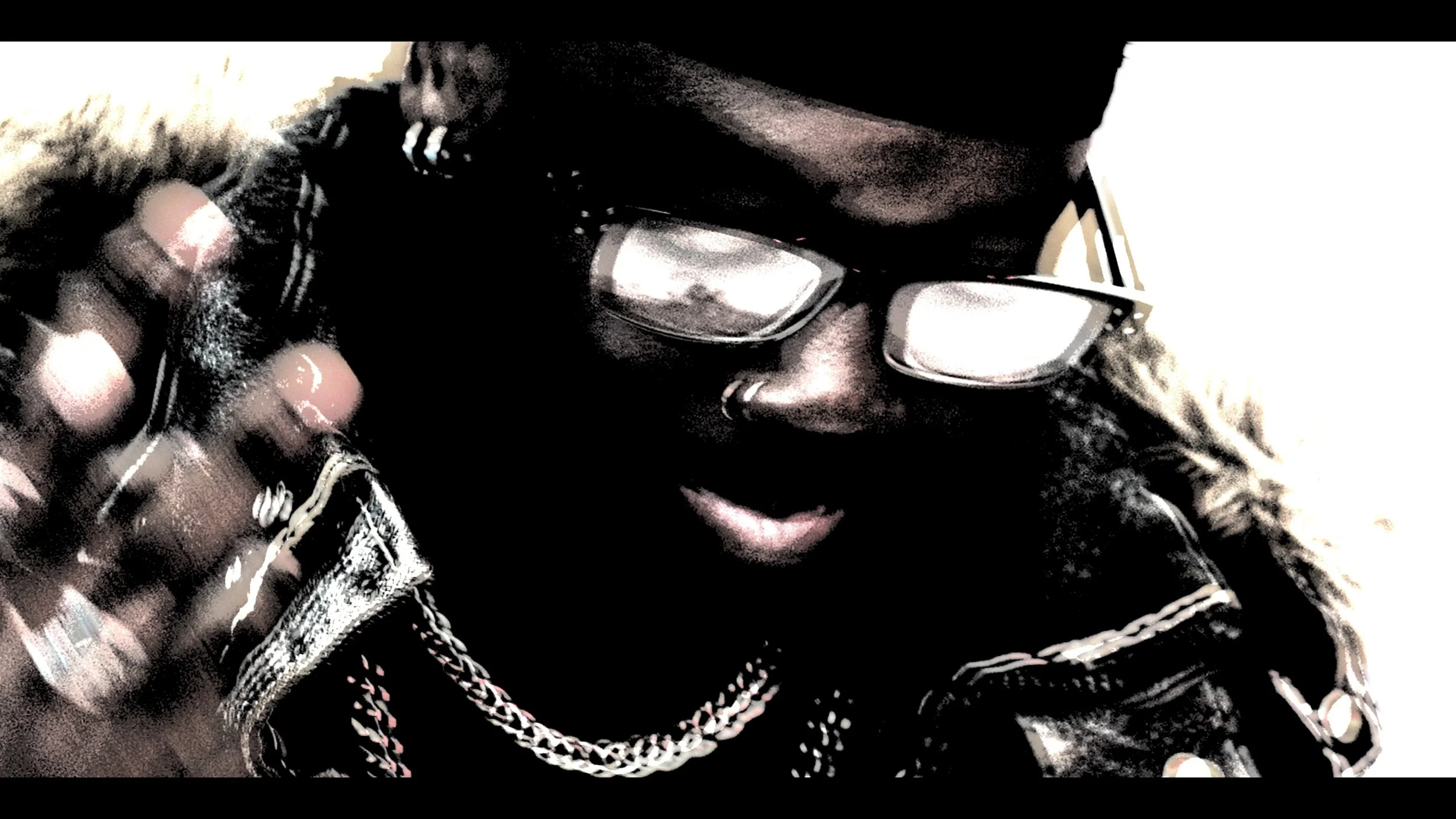 Close-up of a person wearing glasses, a black beanie, and a fur-lined jacket, with rings and chains, speaking on a phone.