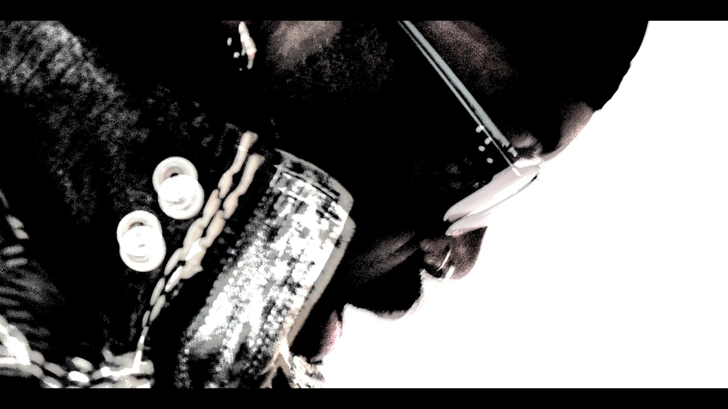 Close-up of a person wearing sunglasses, holding a glass bottle near their mouth, with a chain around their neck and a focus on the side profile against a white background.