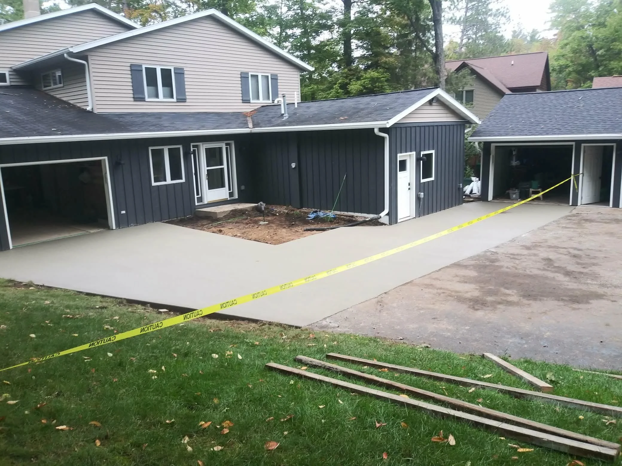 New concrete driveway being poured in front of a house, with caution tape and construction materials nearby.