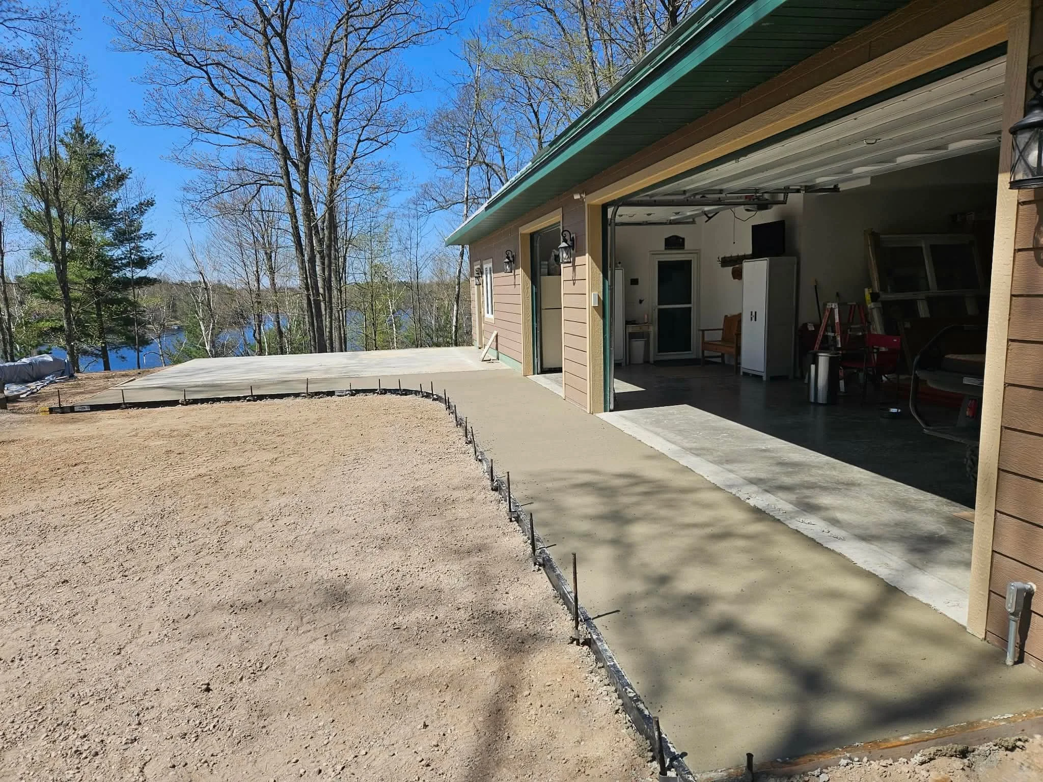 Backyard with a new concrete patio beside a garage, overlooking a lake and trees.