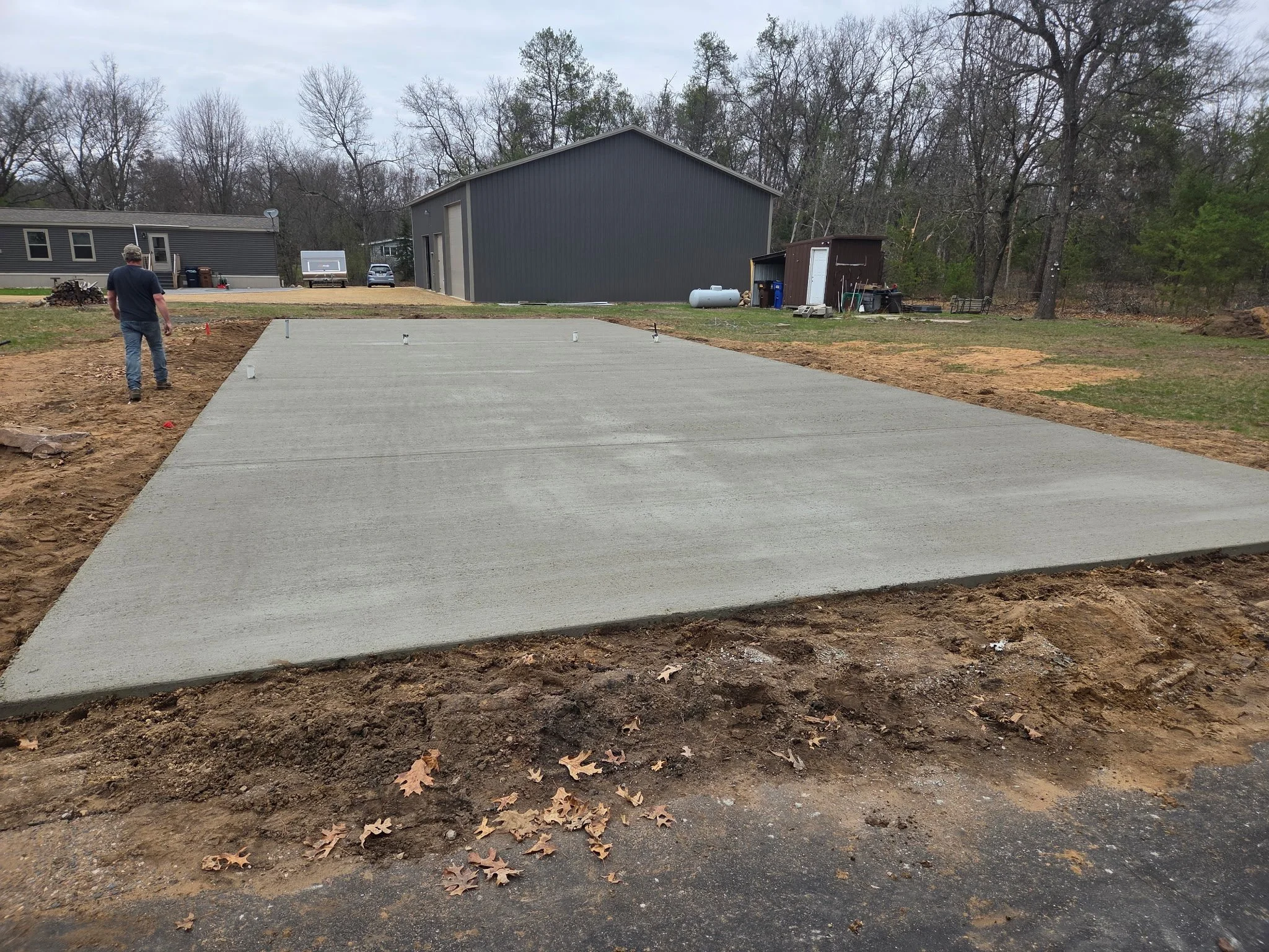 Freshly poured concrete slab with a person walking nearby on a construction site in a suburban area.
