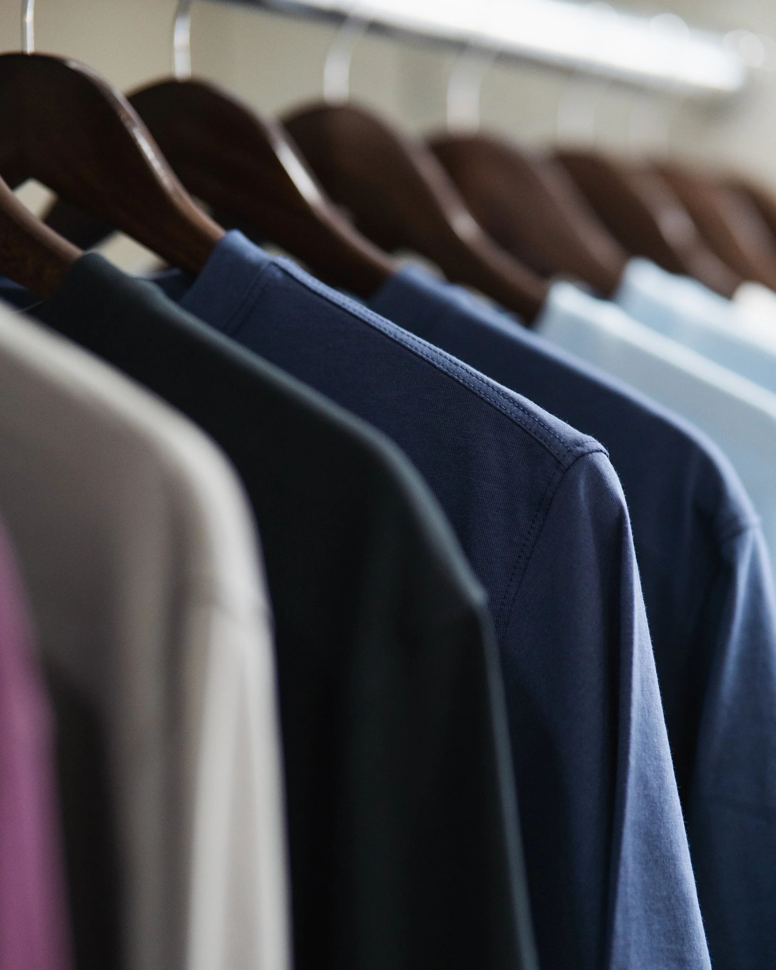 Close-up of various colored clothes hanging on wooden hangers on a metal rack, focusing on the clothing fabric.