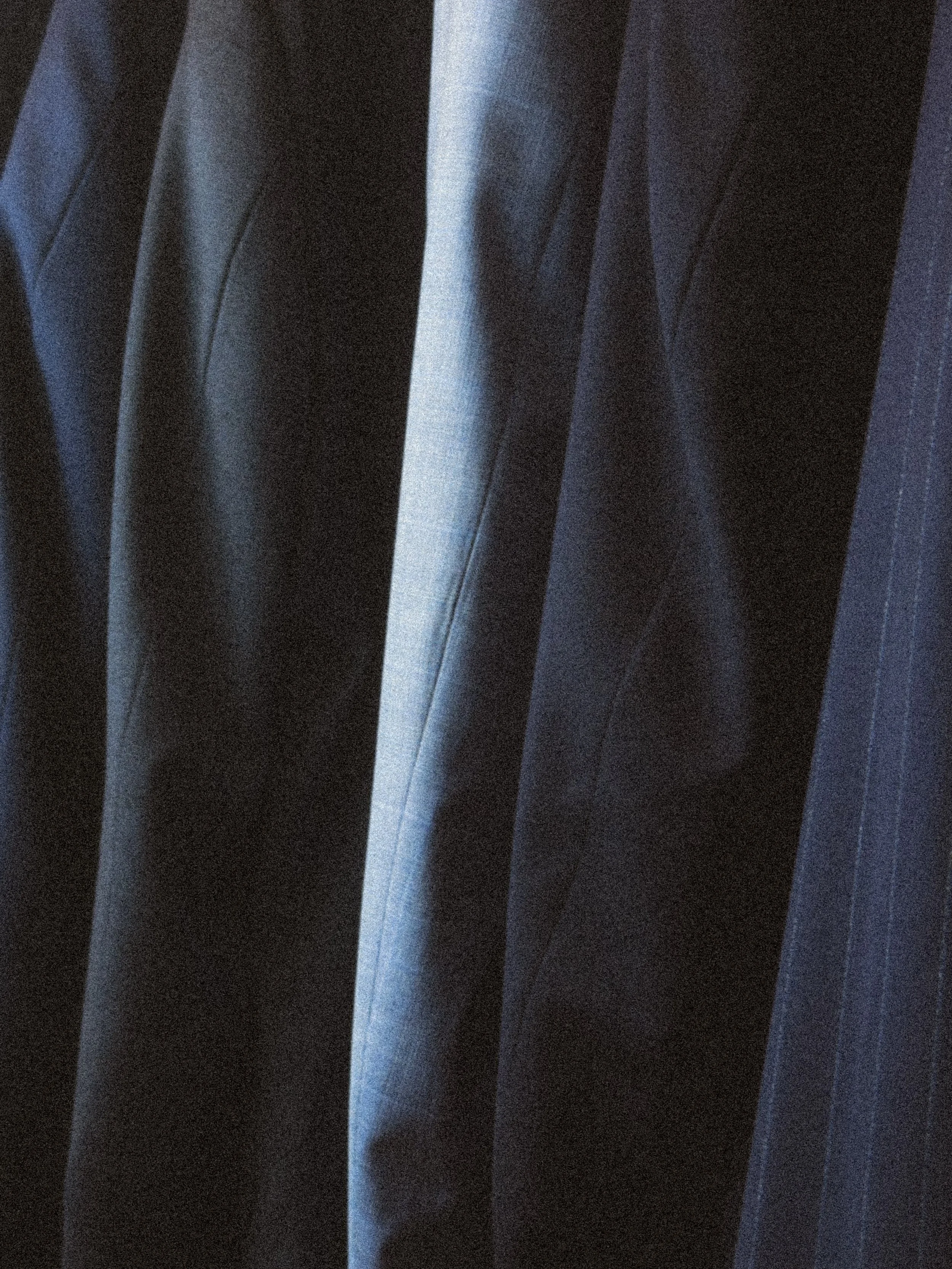 Close-up of dark suits hanging on a rack in a clothing store.