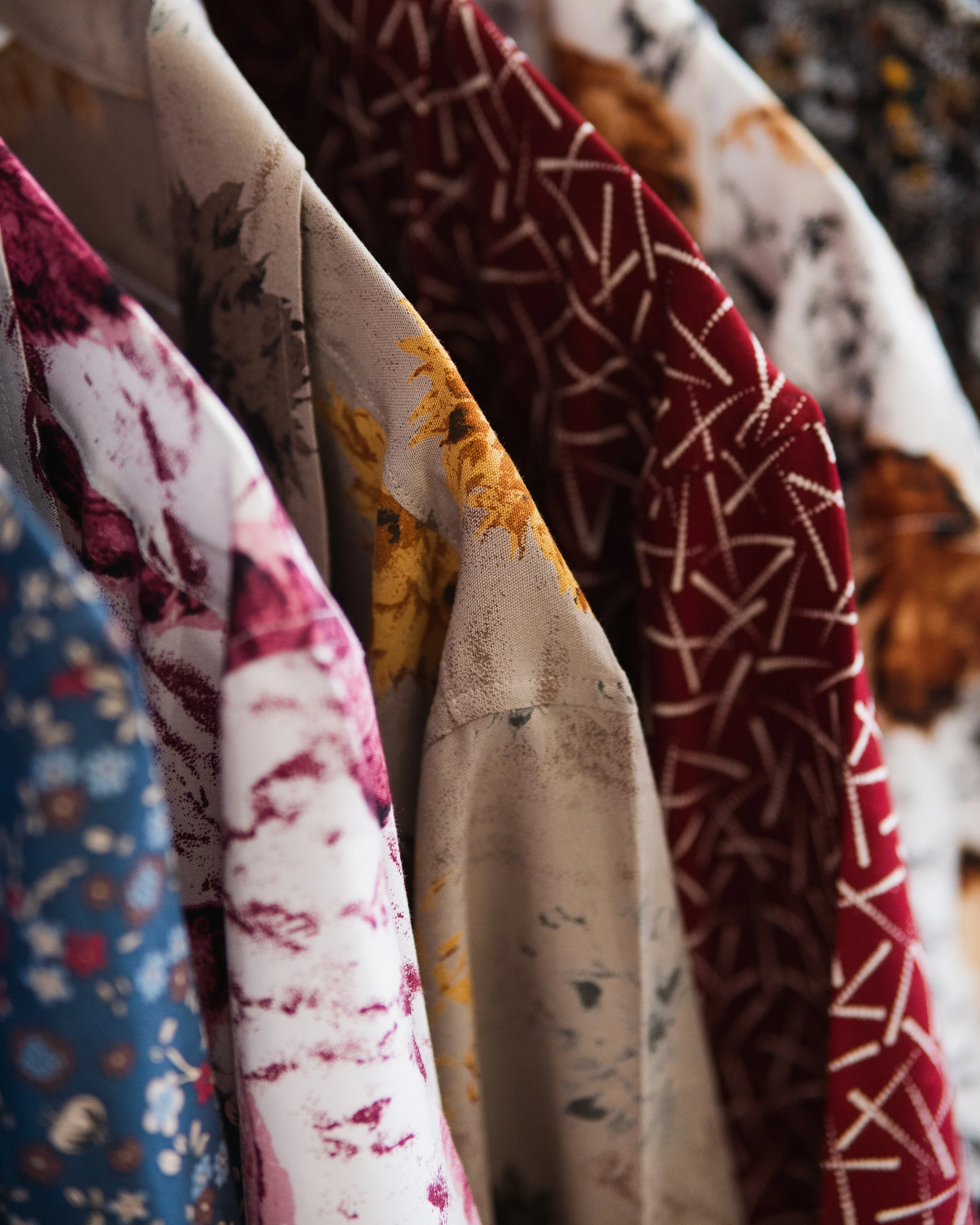 Close-up of casual t-shirts with fabric in various floral and geometric patterns hanging side by side.