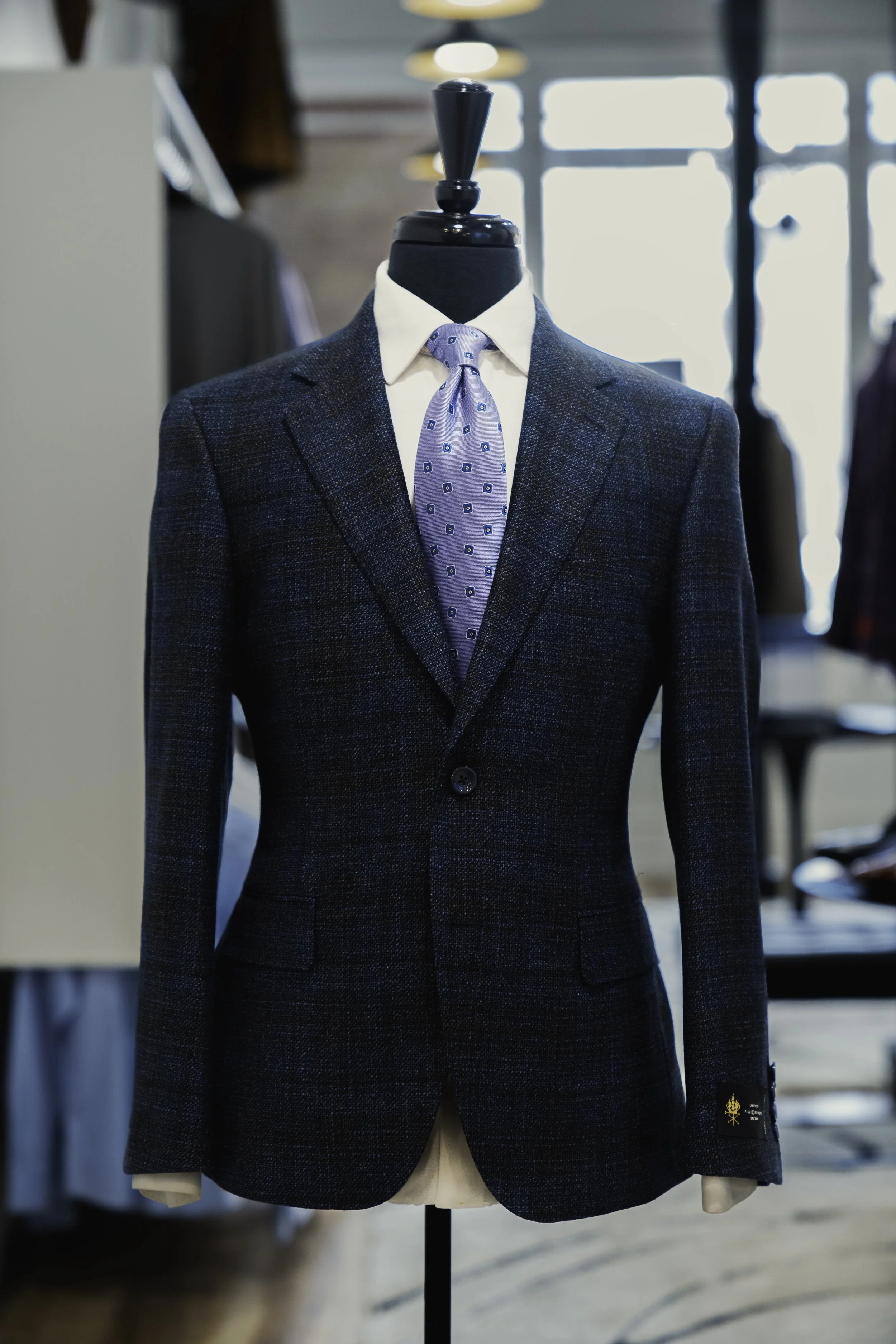 Close-up of a mannequin wearing a dark plaid blazer, white shirt, and light blue patterned tie in a clothing store.