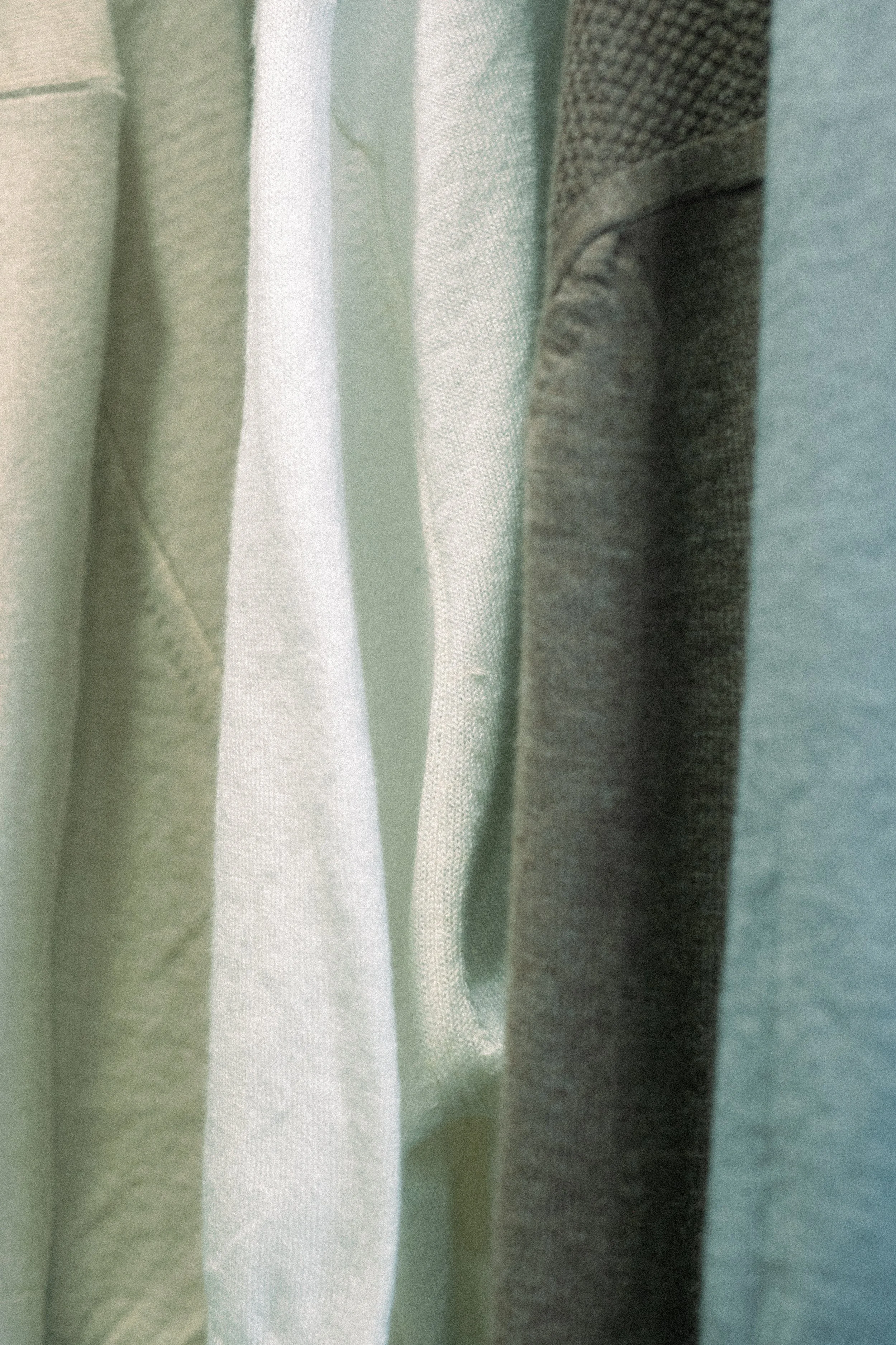 Close-up of various knit shirts in neutral tones hanging on a rack.