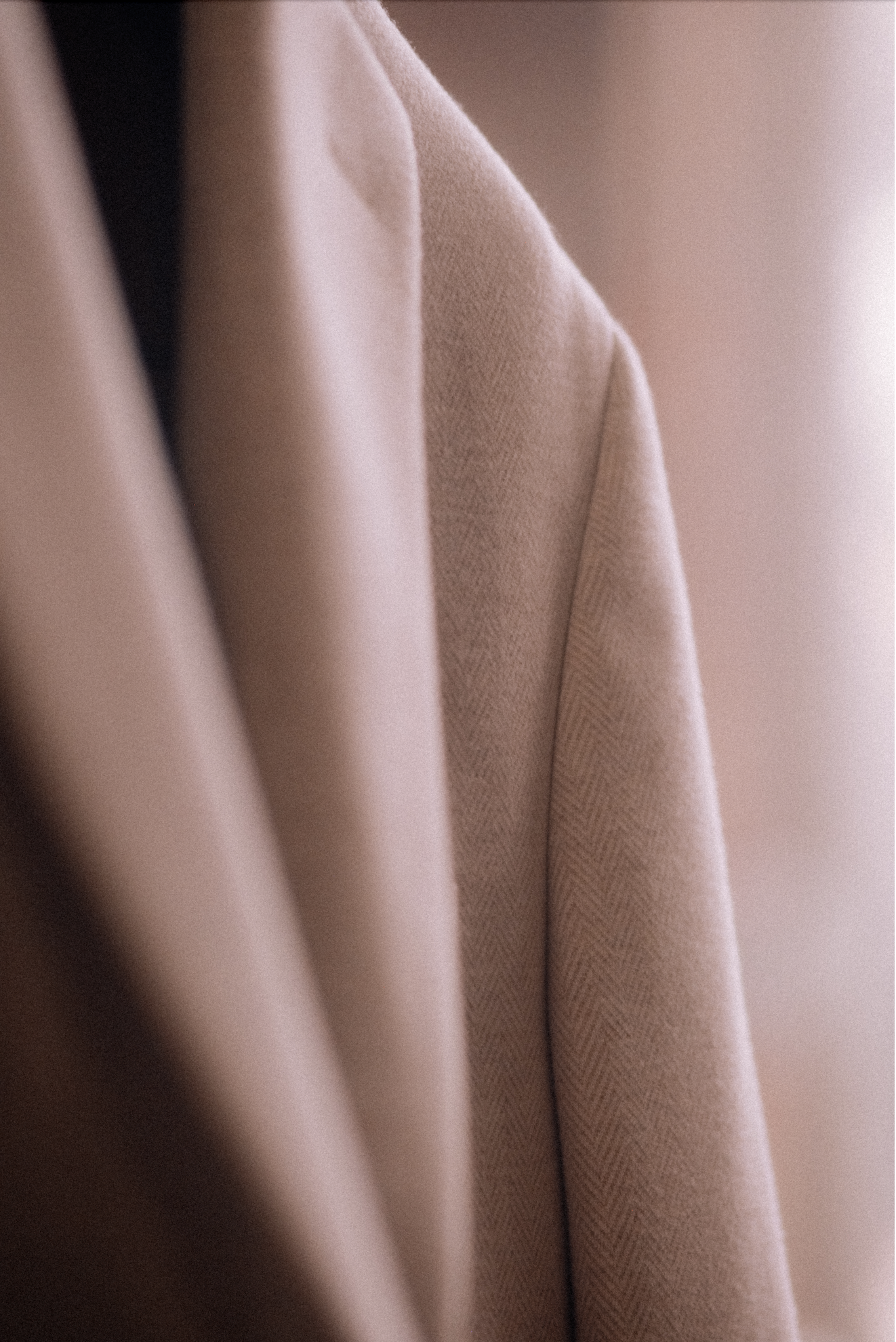 Close-up of beige/off white sport coat hanging near a window with natural light.