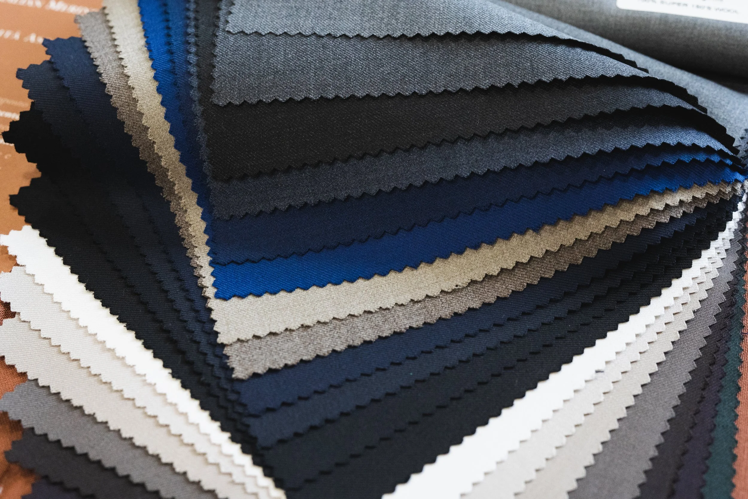 Stack of fabric swatches in various shades of blue, gray, black, and white, with zigzag edges.