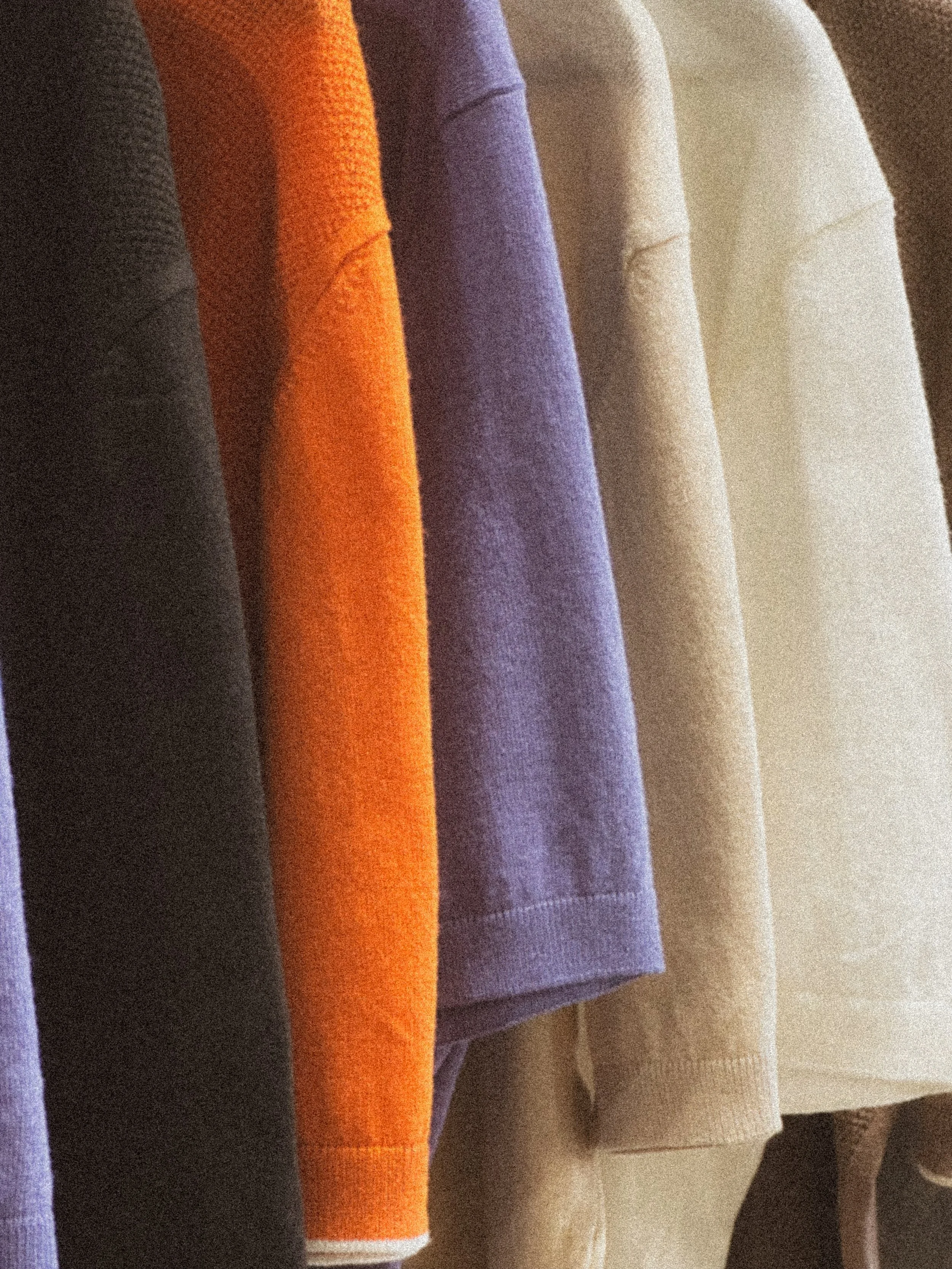 Close up of multiple knit shirts in various colors hanging on a rack in a clothing store.