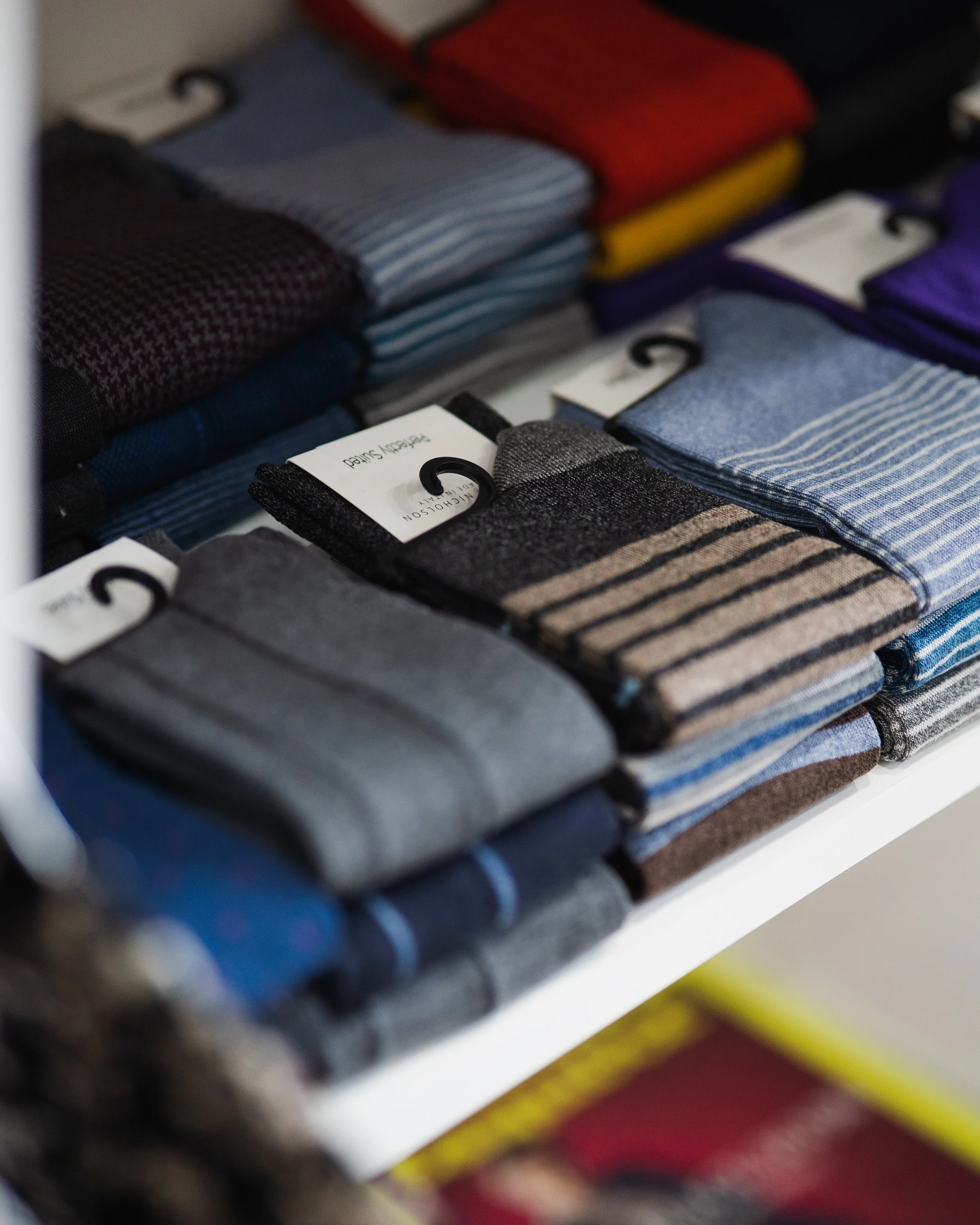Various men's socks displayed on a store shelf, including different colors and patterns such as striped, checkered, and solid designs.