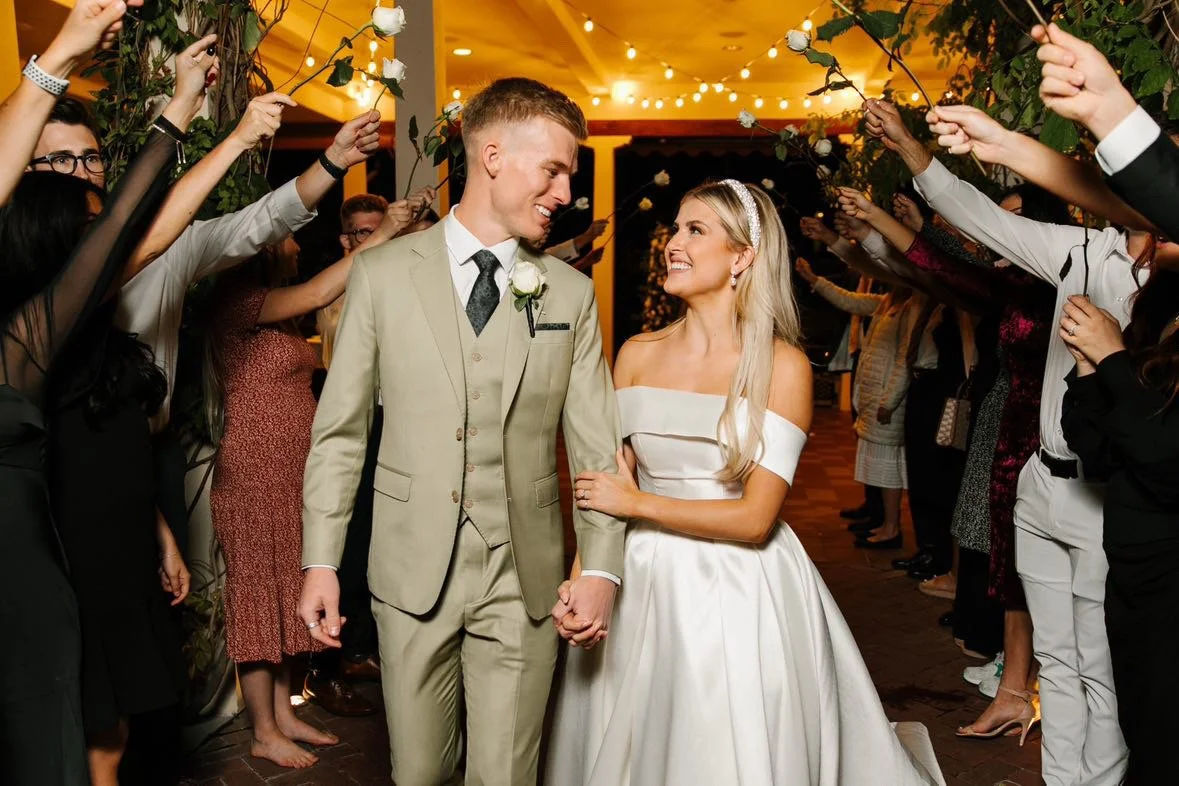 Bride and groom holding hands and smiling at each other during their wedding reception, surrounded by guests holding sparklers.