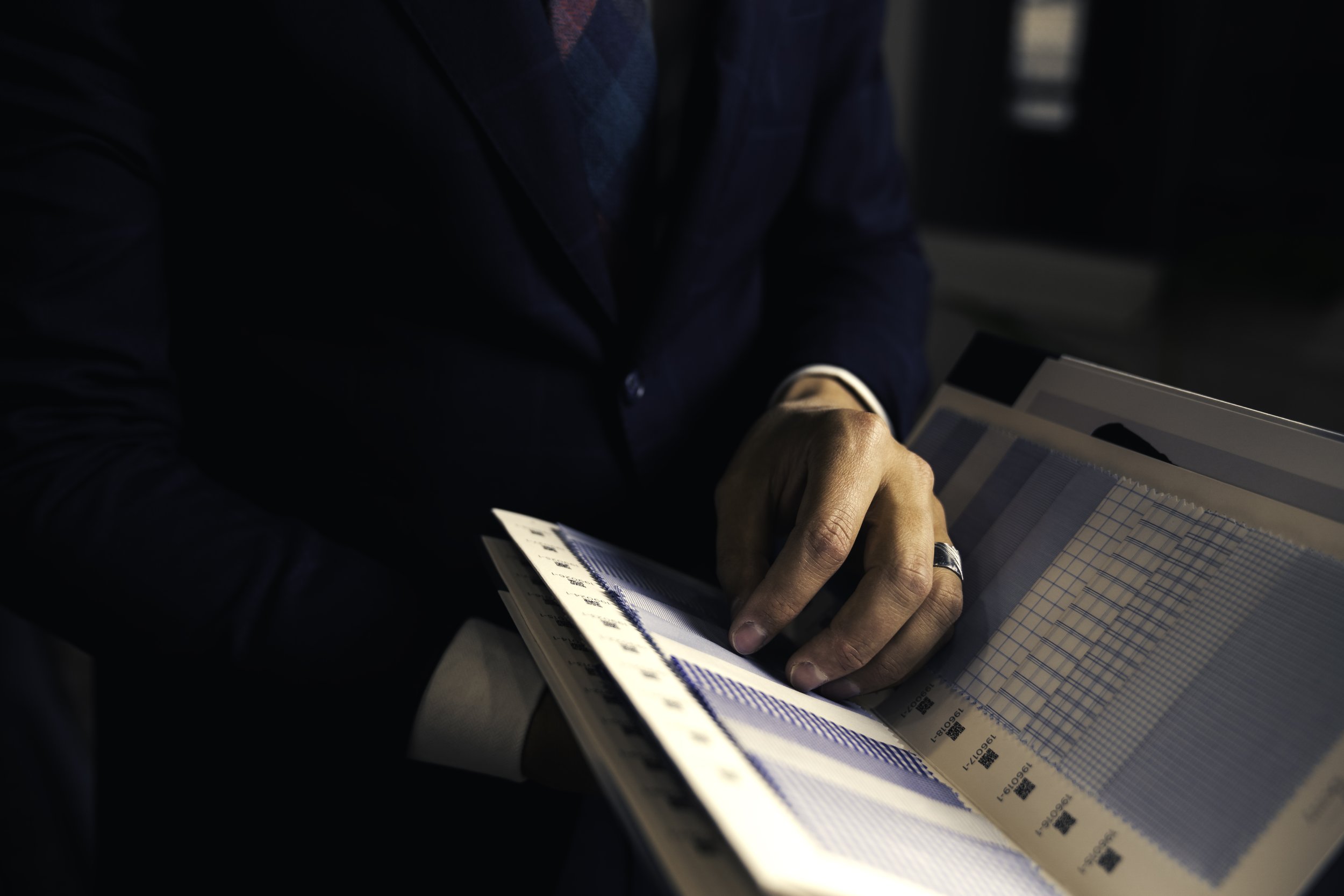 A person wearing a dark blue suit is looking at fabric samples in a custom clothing shop.