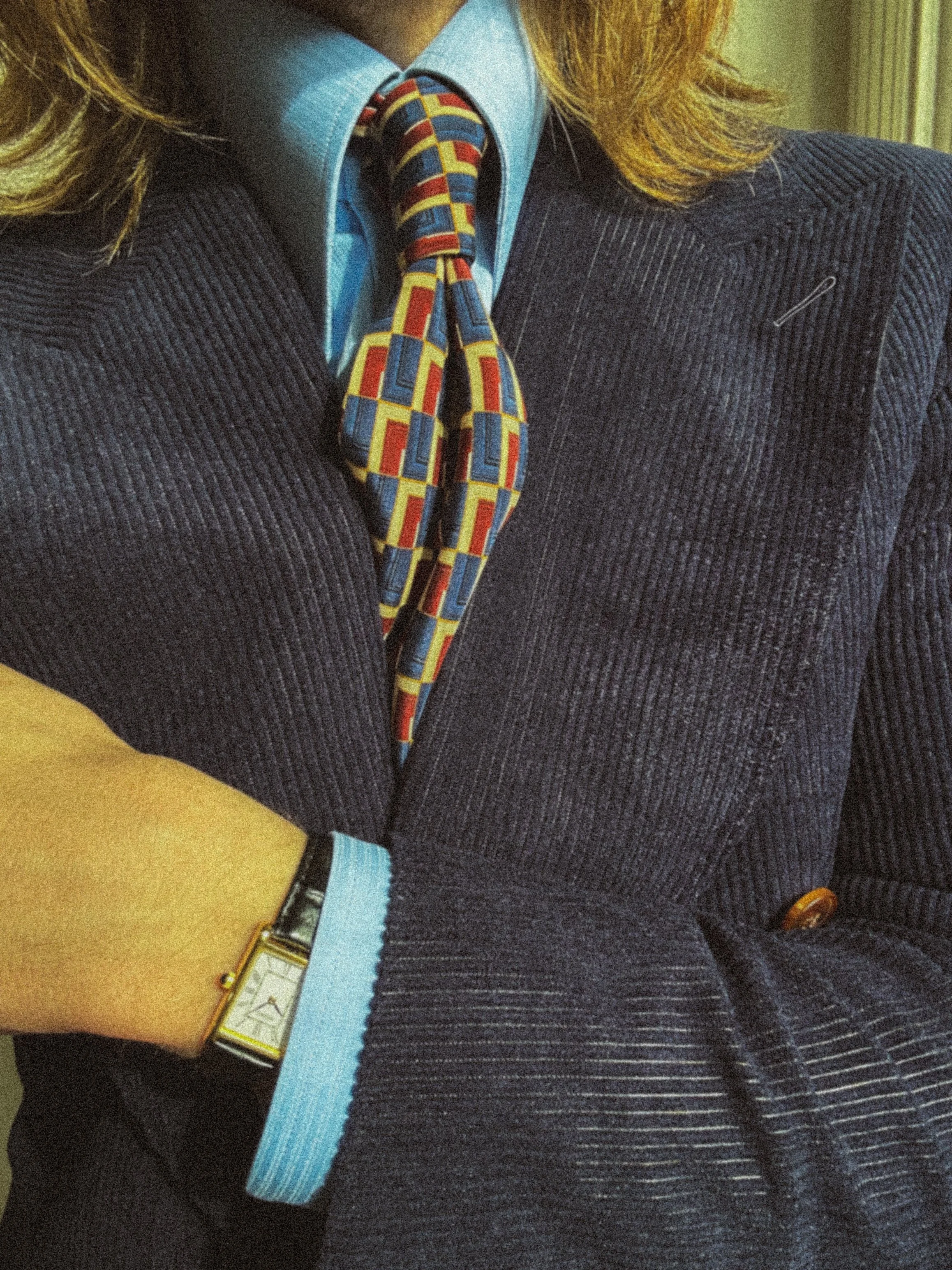 Person wearing a navy corduroy suit, blue dress shirt, colorful patterned tie, and a wristwatch.
