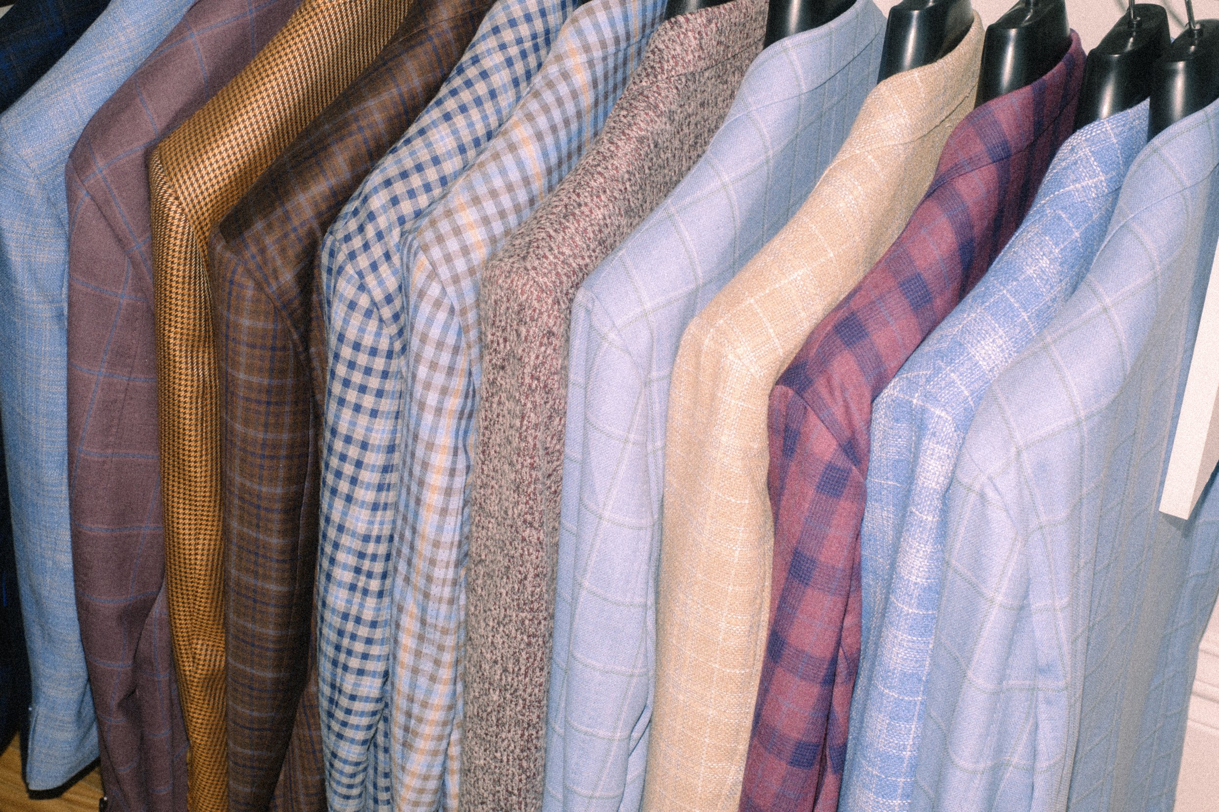 A row of men's sport coats with various patterns and colors on hangers.
