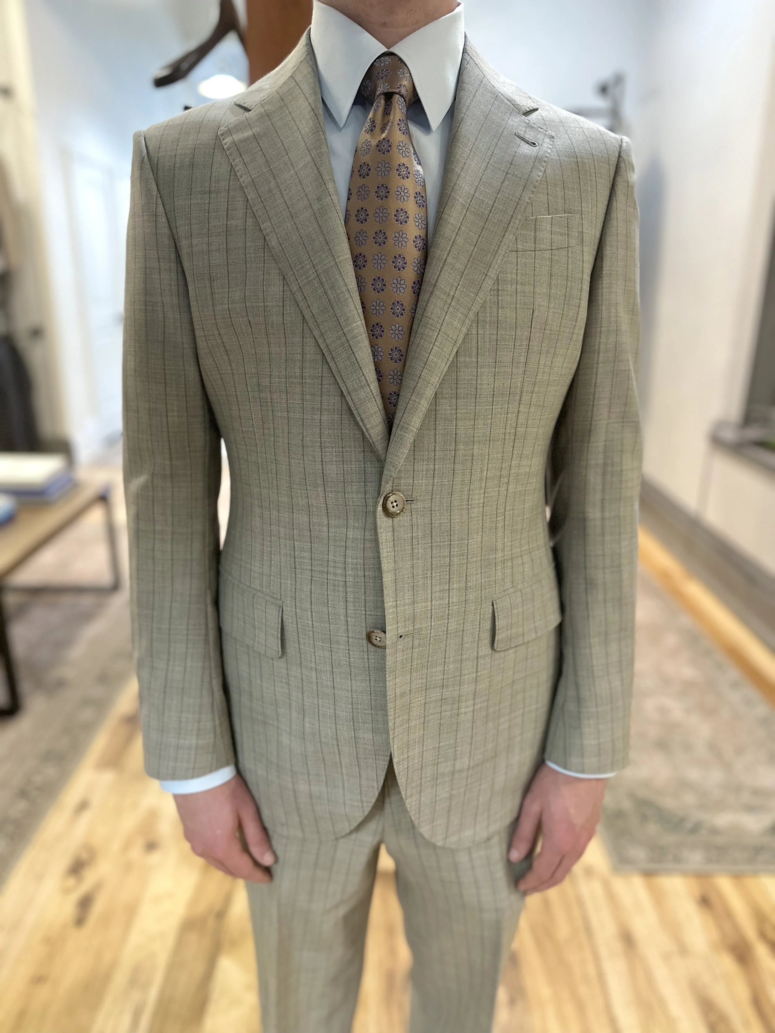 A man is wearing a classic striped suit with a notch lapel and two buttons, paired with a white dress shirt and a patterned tie.