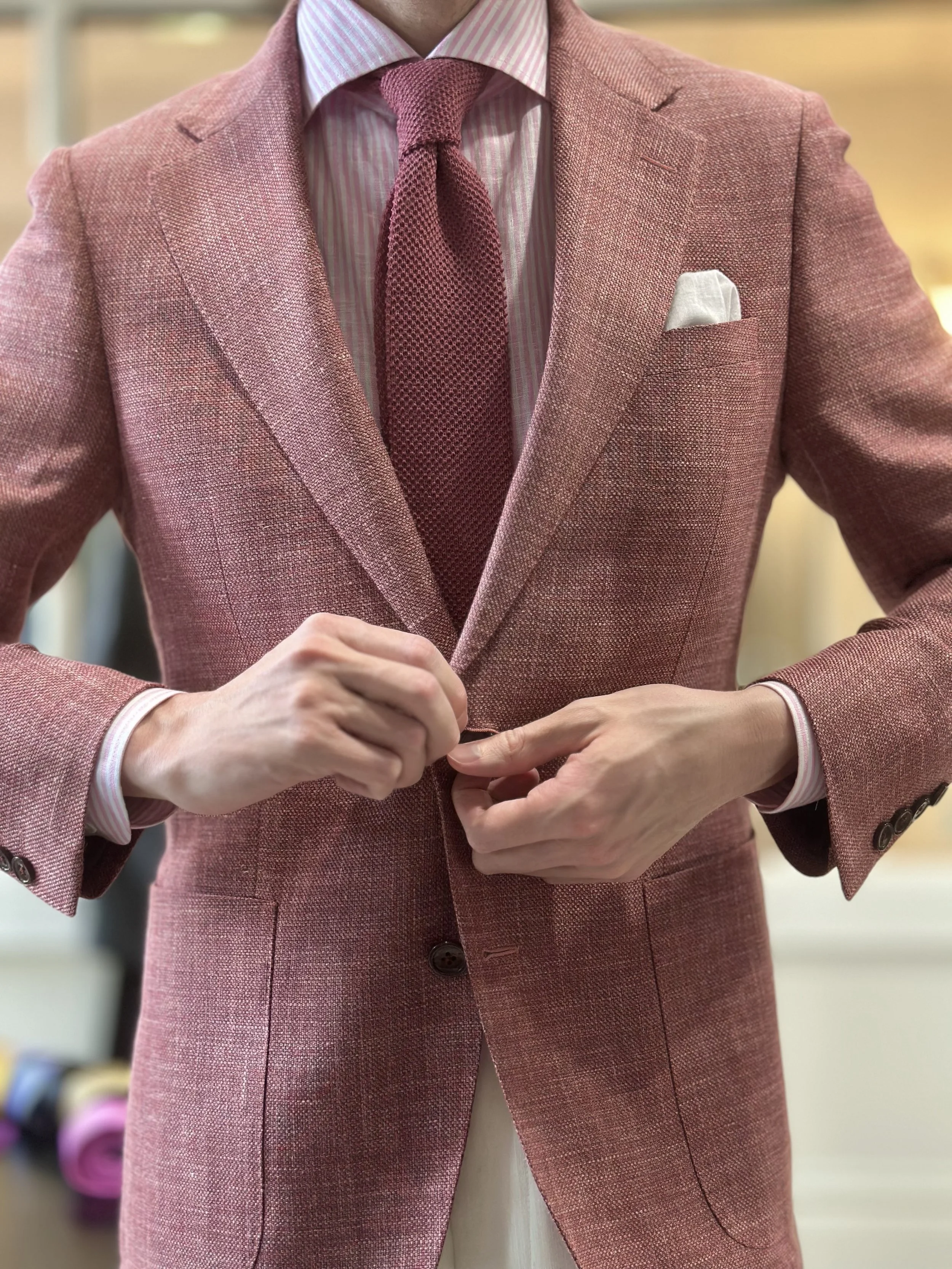 Person adjusting a pink blazer with a white pocket square, wearing a pink tie and a pink striped shirt.