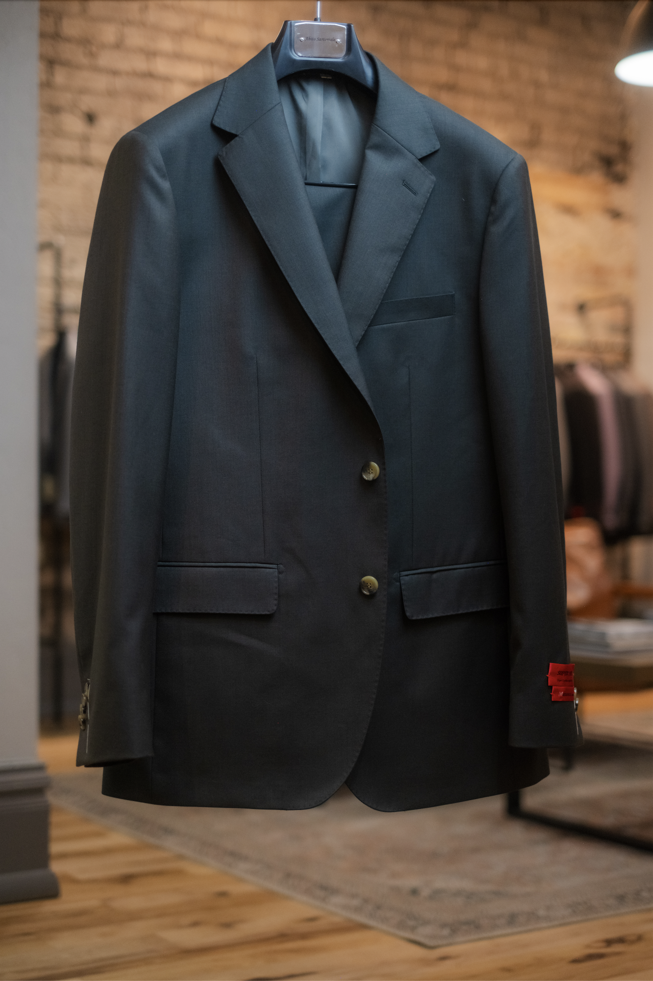 Dark suit jacket hanging on a hanger in a clothing store with a brick wall background.
