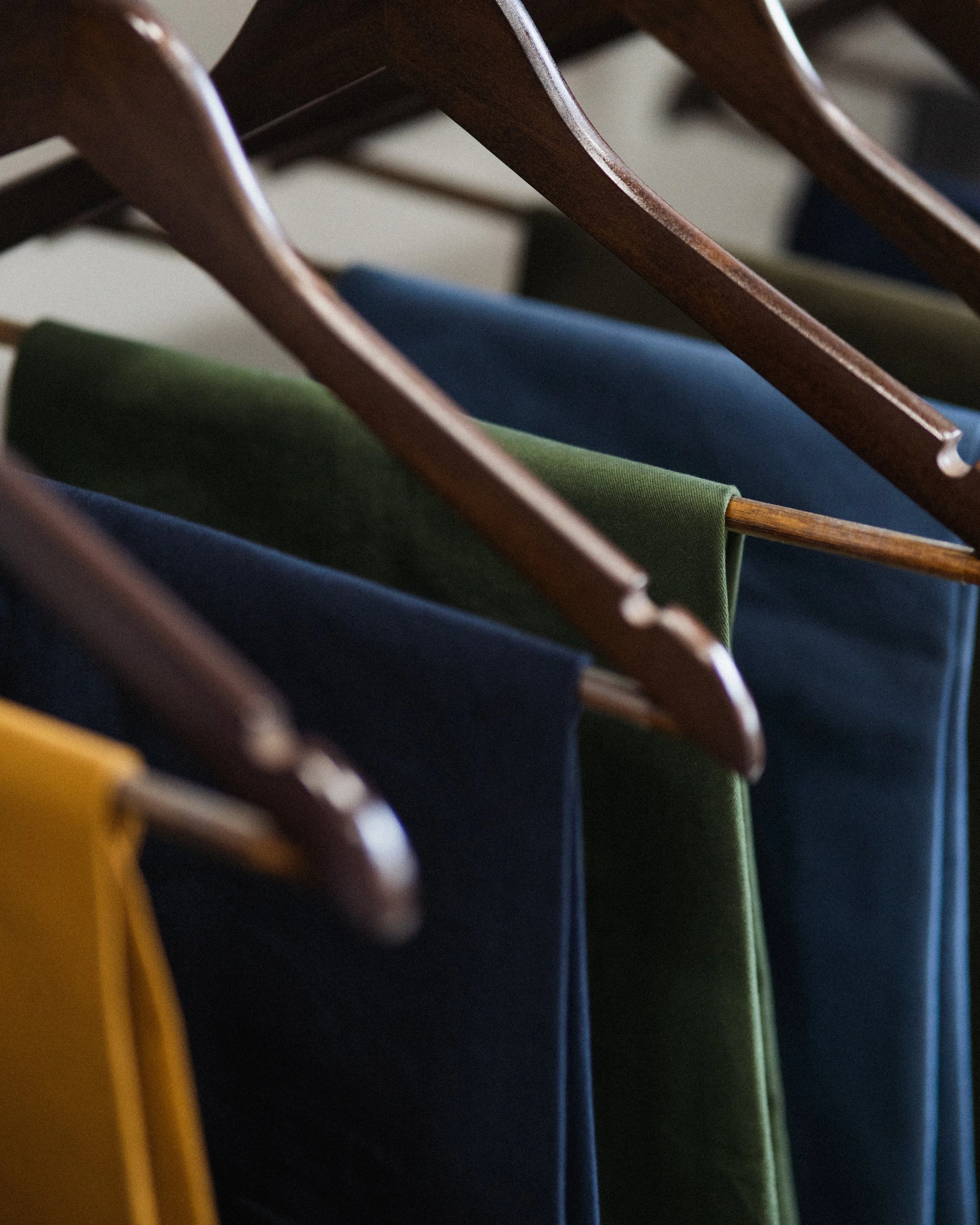 Close-up of colorful pants and chinos, including yellow, green, blue, and gray, arranged on a rack on hangers.