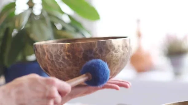 Close-up of a hand holding a singing bowl with a mallet with a blue felt tip.