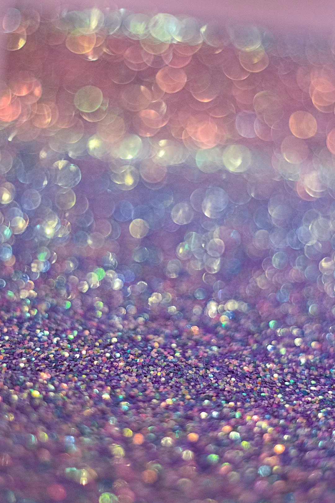 Close-up of iridescent glitter particles with a pink and purple background, creating a dreamy, sparkling effect.