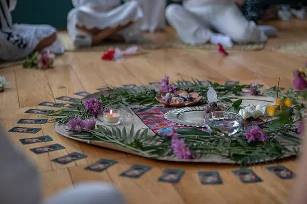 A spiritual altar setup on a wooden floor, featuring candles, flowers, crystals, and photographs arranged in a circular pattern.