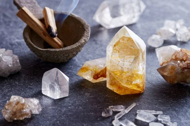 Various quartz crystals and stones on a dark surface, with a small bowl of matches in the background.