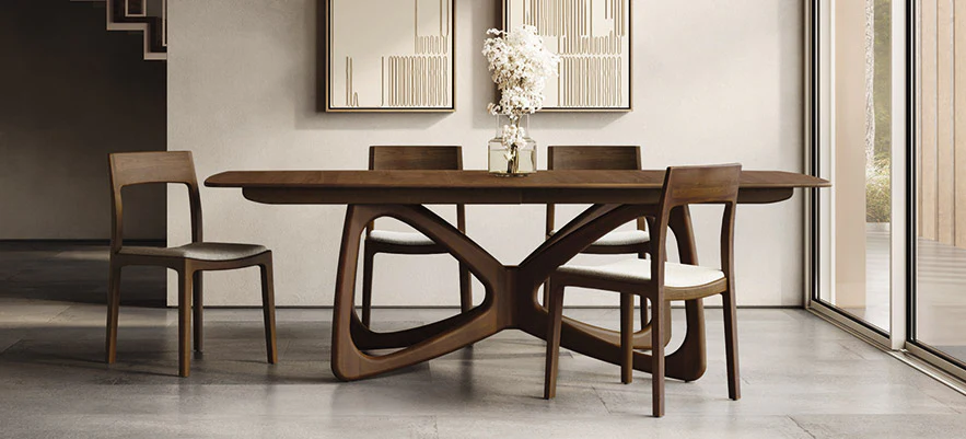 Modern wooden dining table with four chairs and a white floral centerpiece, in a room with a large sliding glass door and minimal wall art.