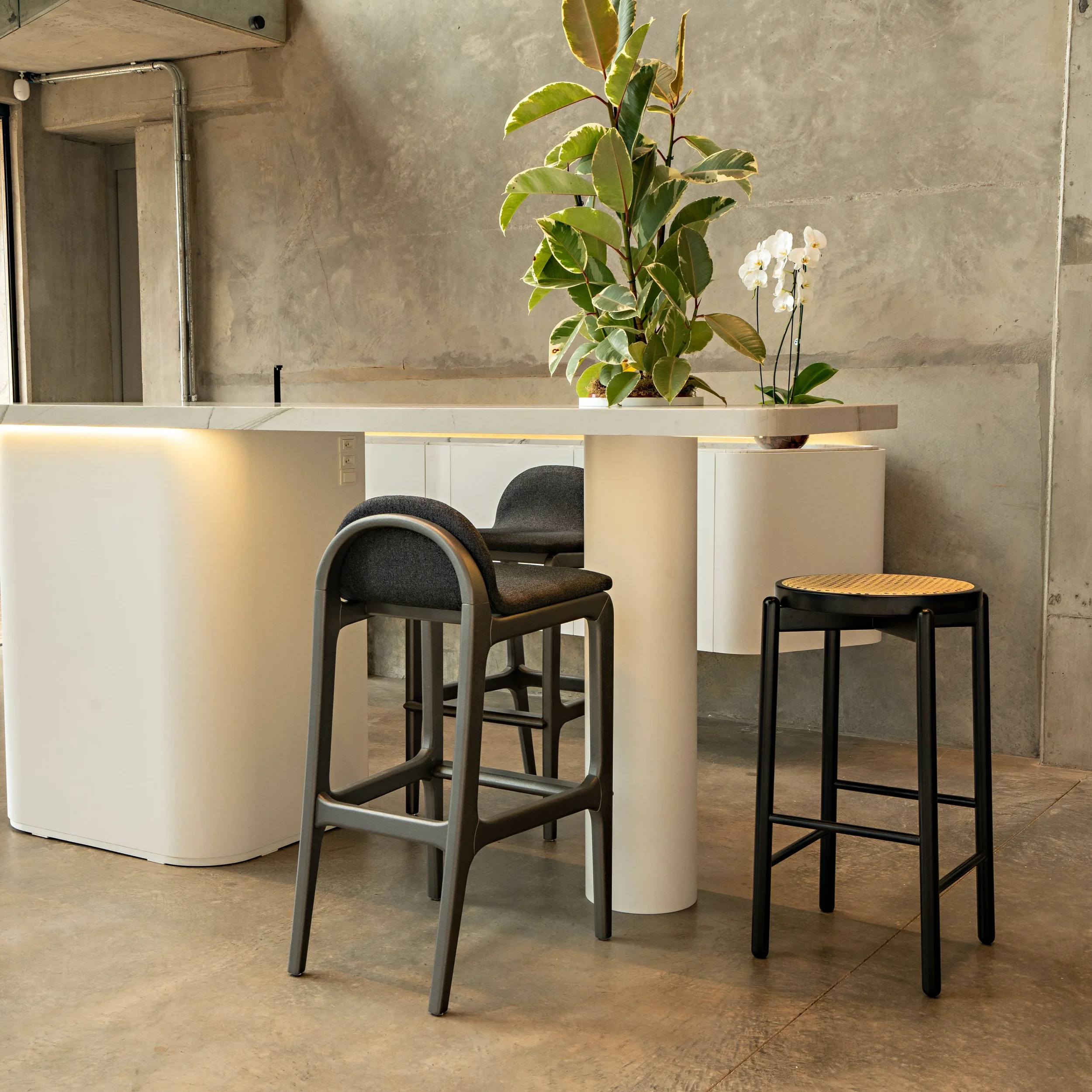 Modern interior with a white high-top table, and two low, rounded back black stools, one with a can seat, by Uultis