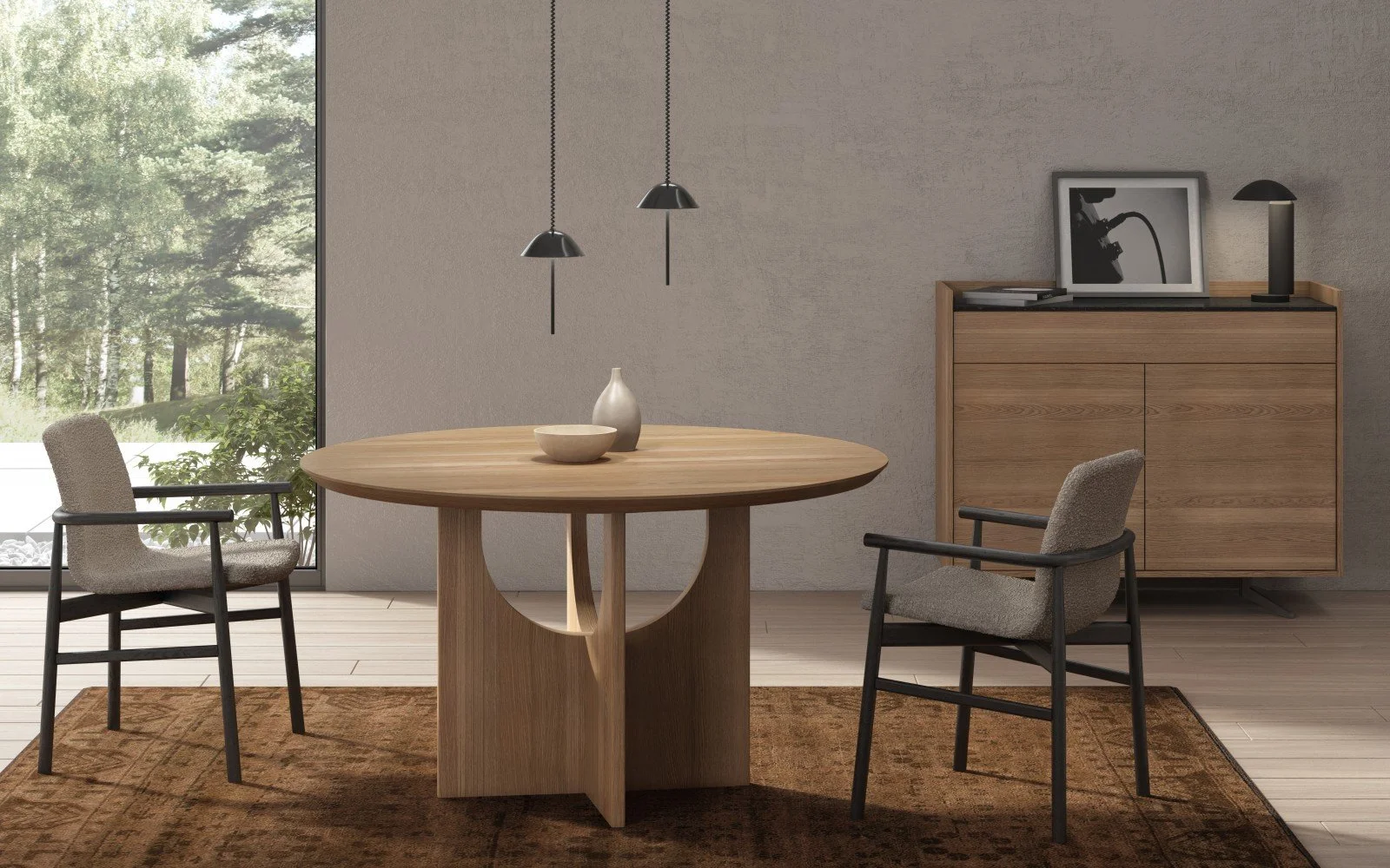 Modern dining room by Huppé with a round wooden table, two upholstered chairs, a sideboard with framed photo and lamp, and large window showing outdoor greenery.