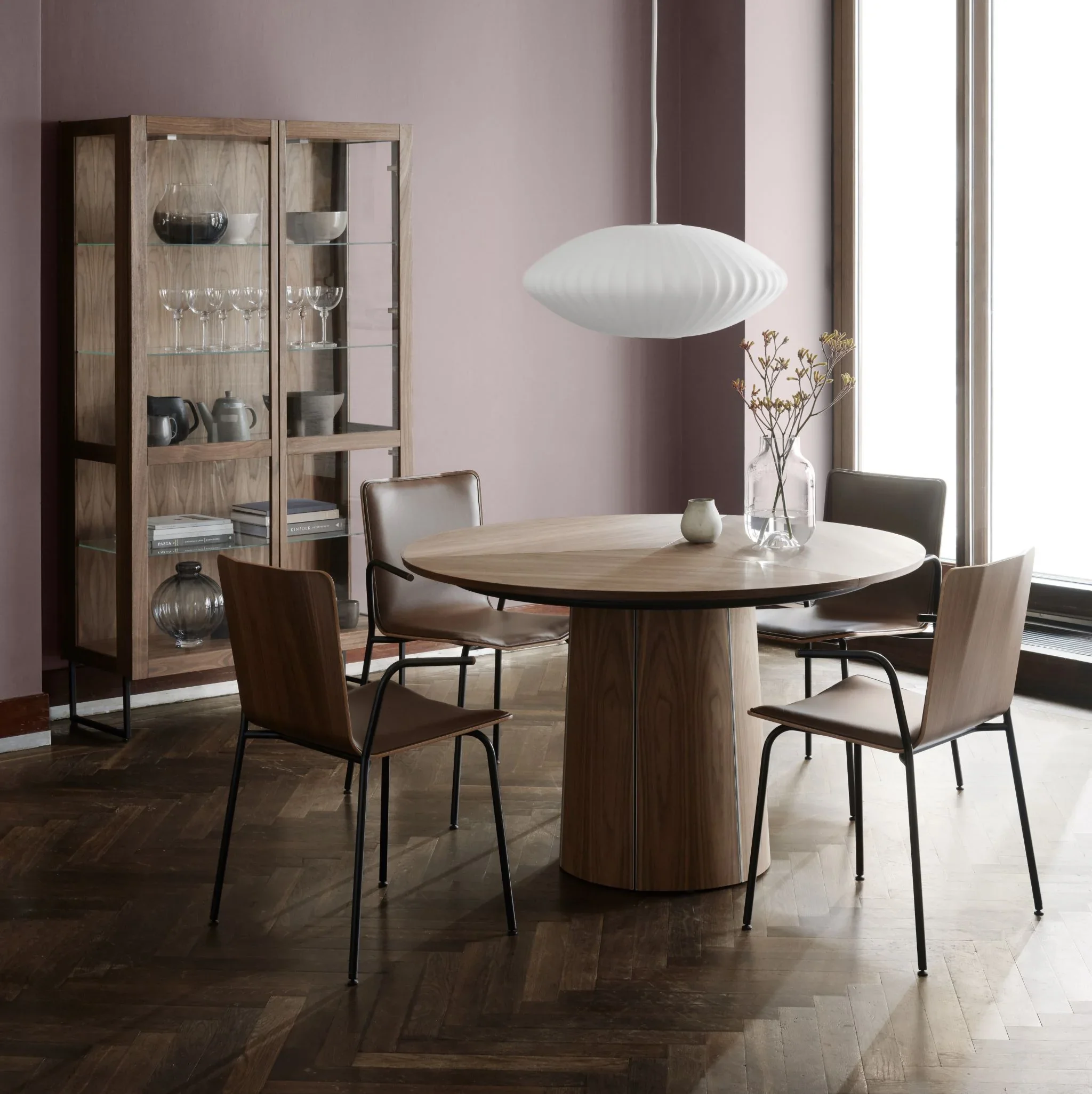 A modern dining room featuring the SM 33, a round wooden extension table, four chairs with metal legs, a wooden display cabinet with glass doors by Skovby