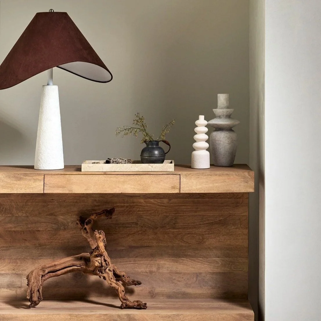 Decorative tabletop with a table lamp, small vases, and a tray with small objects, set on a wooden surface, against a light-colored wall.