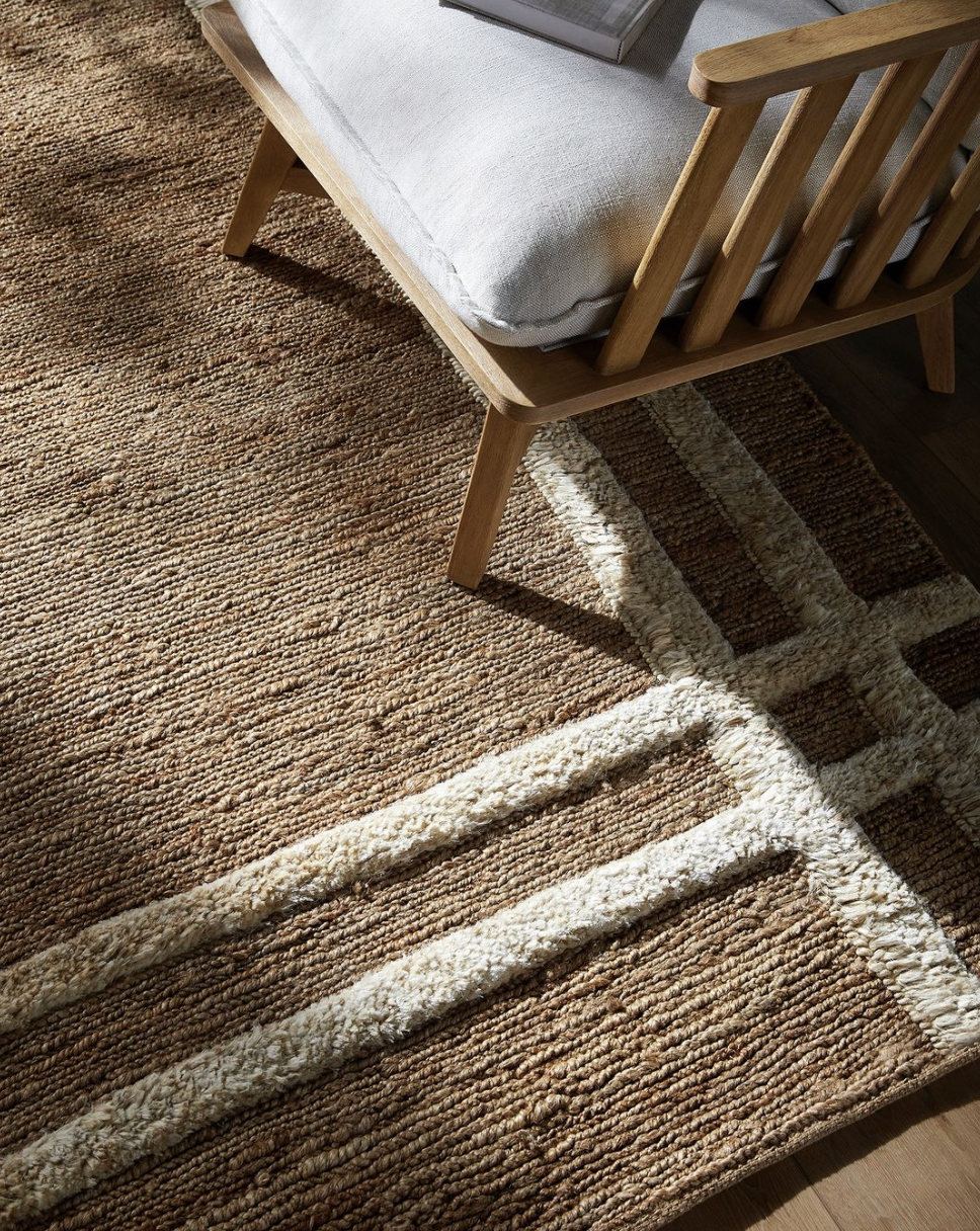 Close-up of a beige and brown textured rug on a wooden floor, under a wooden bed frame with a white mattress and a book on top.