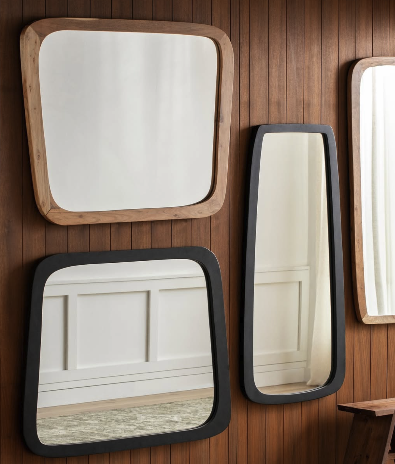 A wall decorated with four mirrors of various shapes and sizes, framed with wood and black borders, mounted on a wooden-paneled wall.