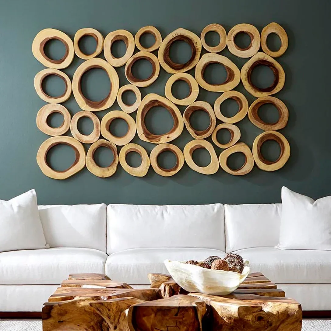 Decorative wall art made of multiple wooden rings of varying sizes arranged on a green wall, above a white sofa and a wooden coffee table with a bowl of decorative stones.