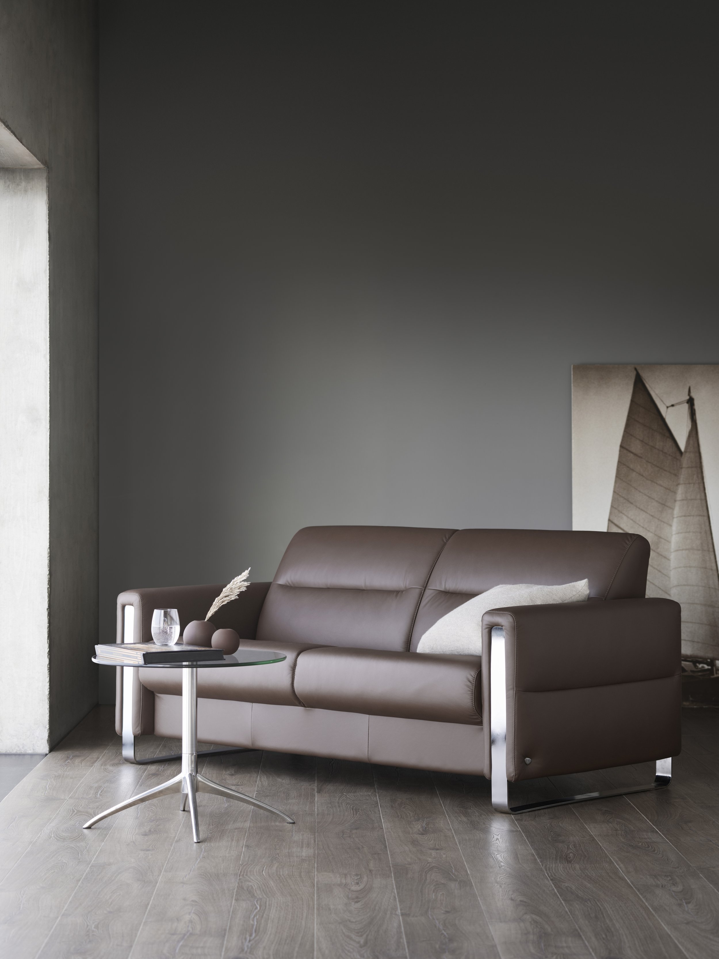 Modern living room with brown leather sofa by Stressless, glass side table, decorative vases, glass of water, and abstract art