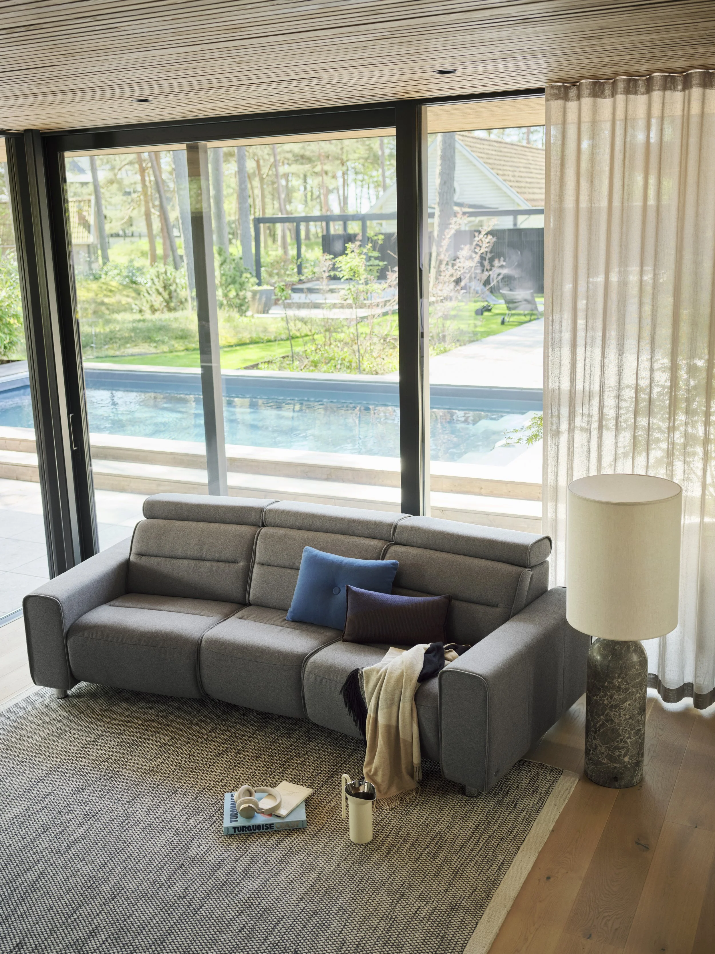 Living room with a curved back gray sofa by Stressless in blue with  dark brown pillows, a blanket, a white mug