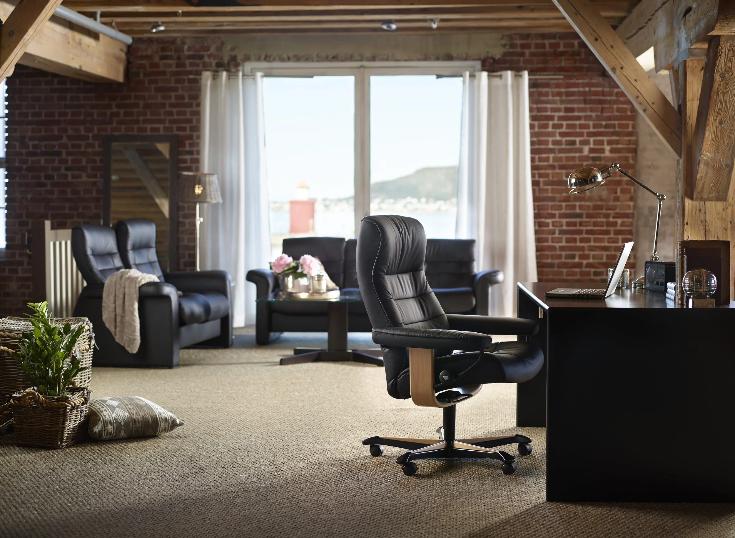 A modern office with a black desk, and an ergonomic black leather Stressless office chair