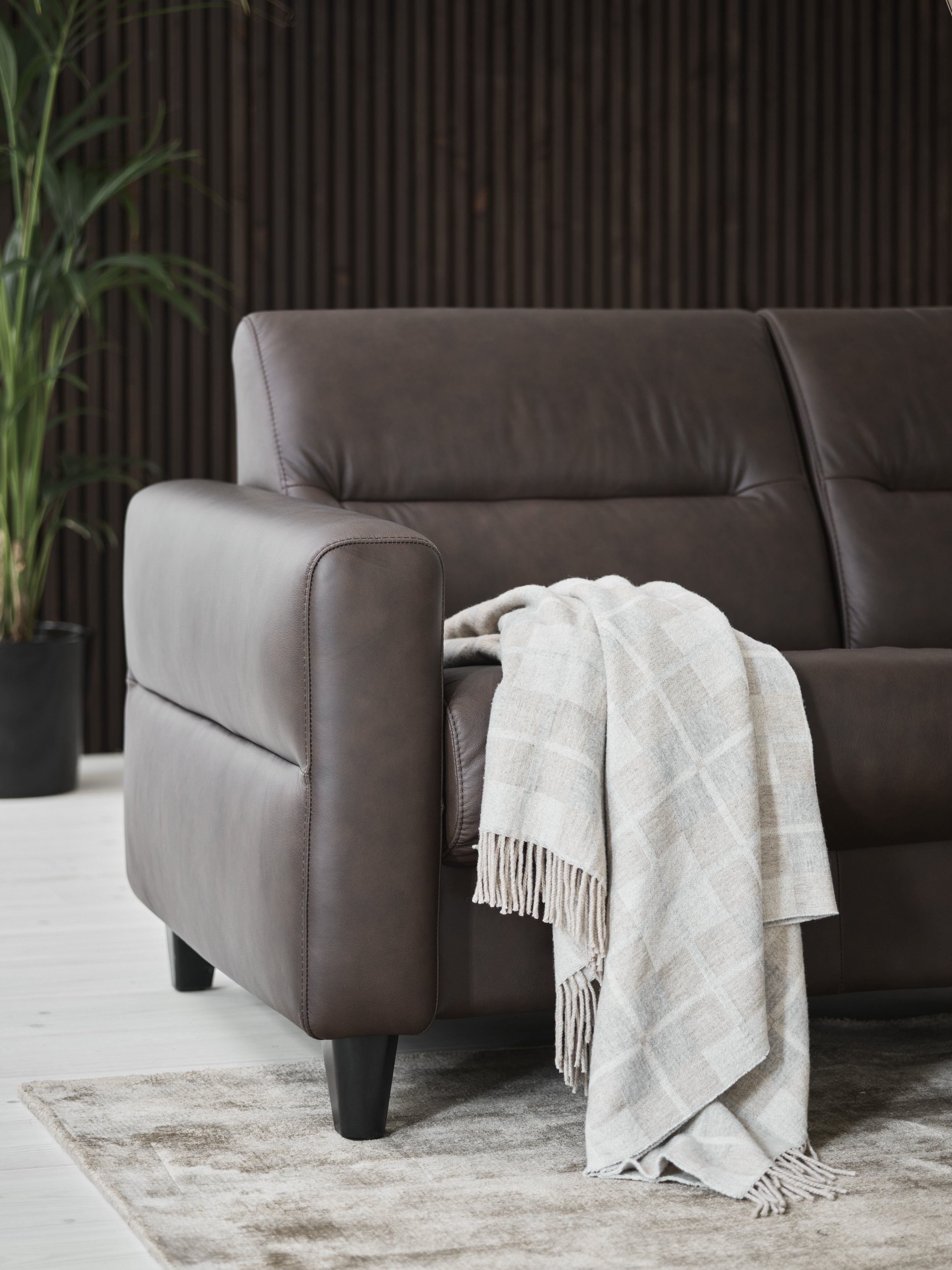 A dark brown leather sofa by Stressless with a light-colored plaid throw blanket hanging over the armrest, in a modern living room 