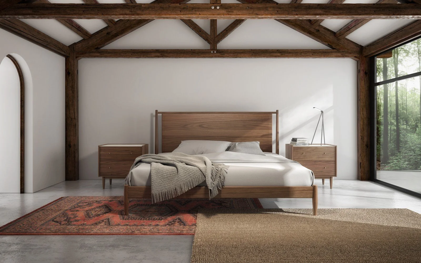 Minimalist bedroom with wooden furniture, white walls, large window revealing trees outside, bed with beige bedding and throw, two nightstands with books and a desk lamp, and area rugs, with exposed wooden ceiling beams.