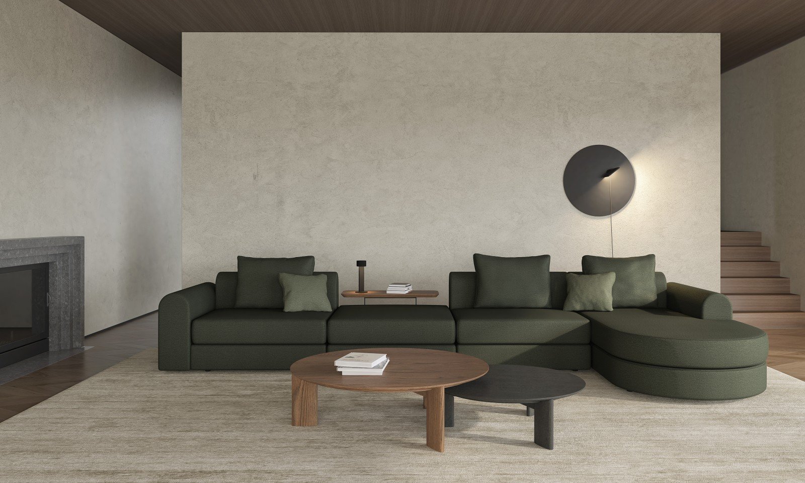 Modern living room with dark green sectional sofa, two small matching pillows, a wooden side table with books, a small black table, a wall-mounted black light fixture, beige walls, wooden stairs on the right, a fireplace on the left, and a beige rug.