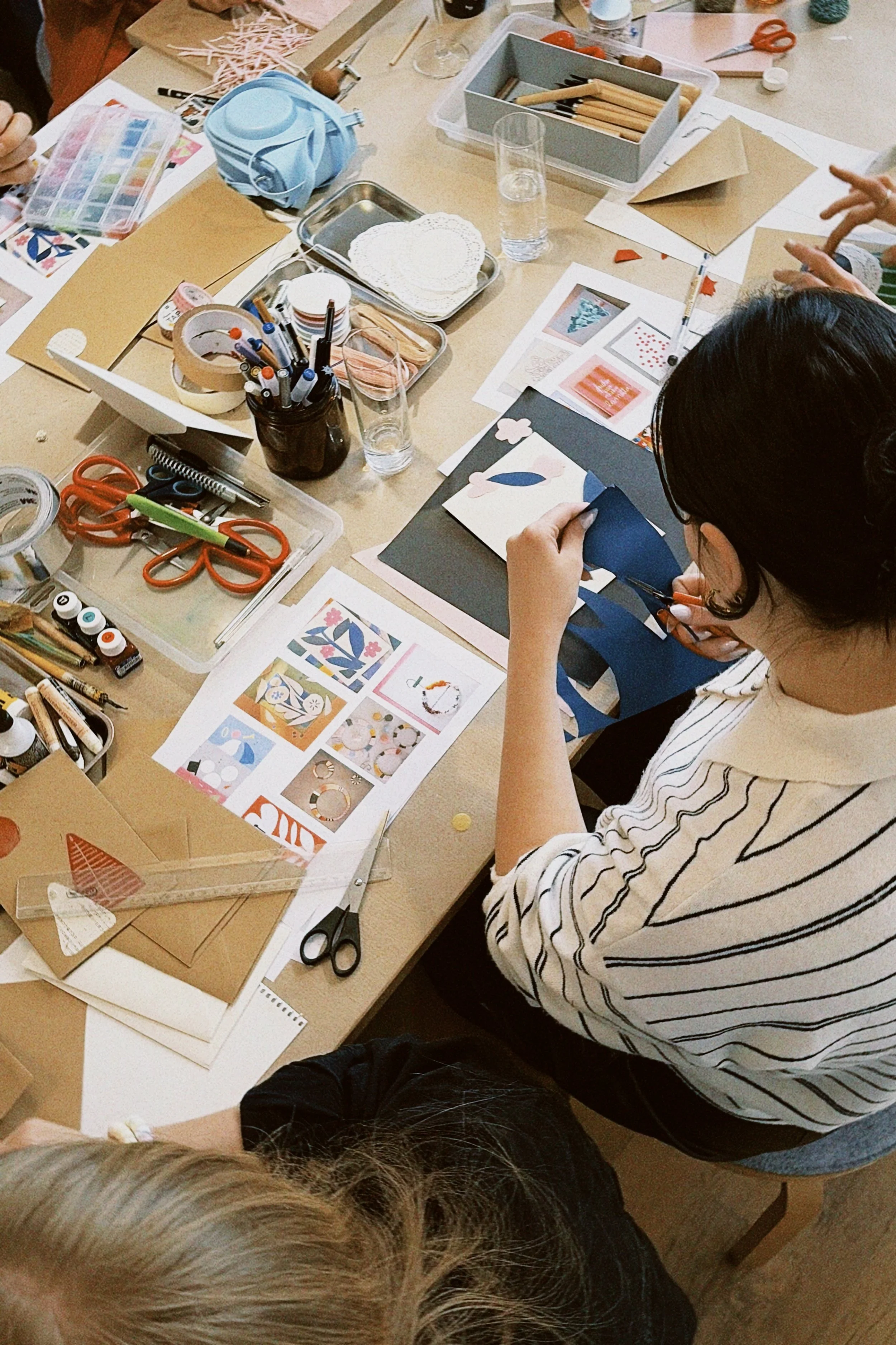 Person beim Basteln mit Papier, Schere und Bastelmaterial auf einem Tisch.