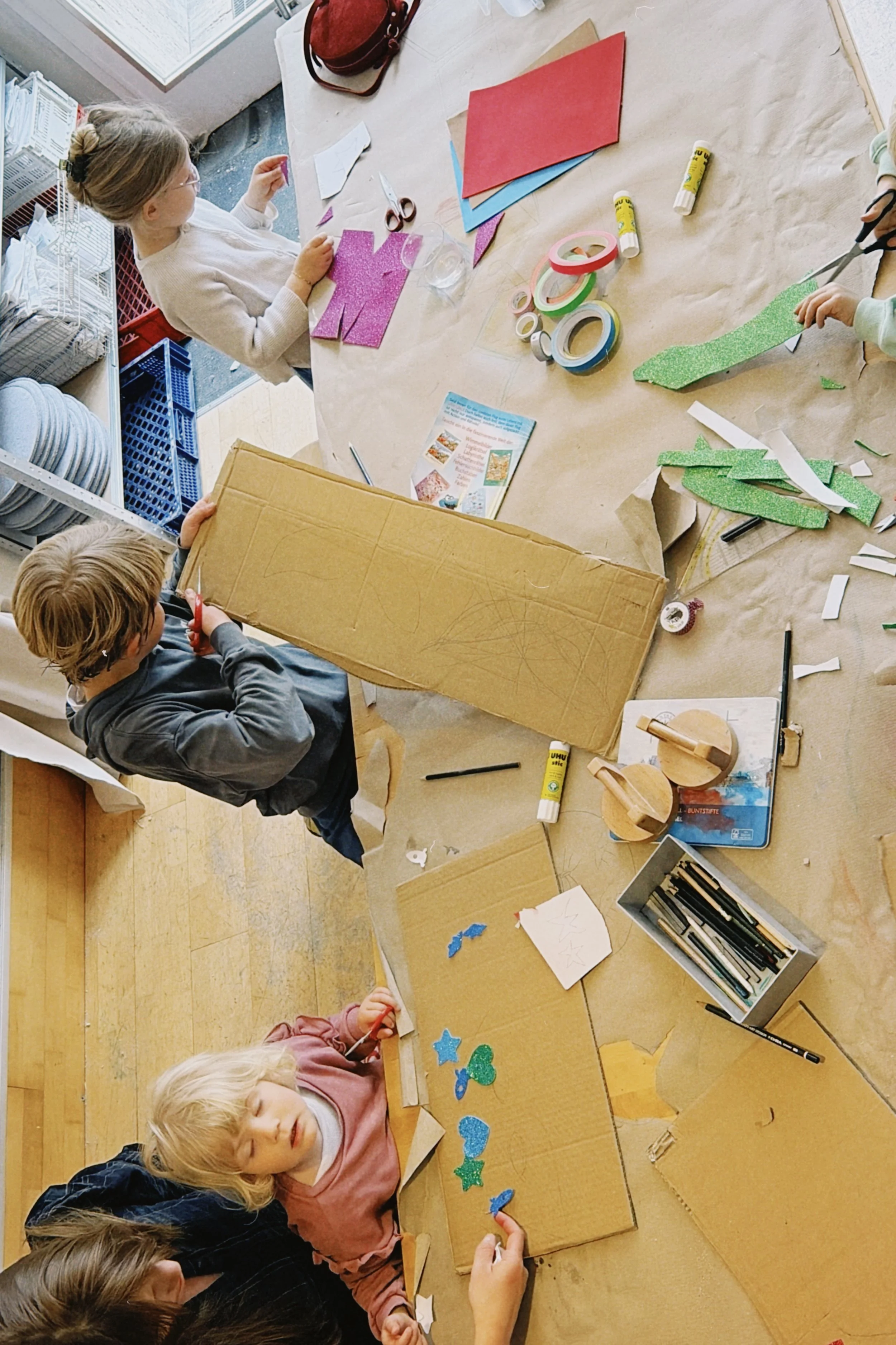 Kinder beim Basteln mit buntem Papier, Scheren, Kleber und Bastelmaterial in einem Raum.