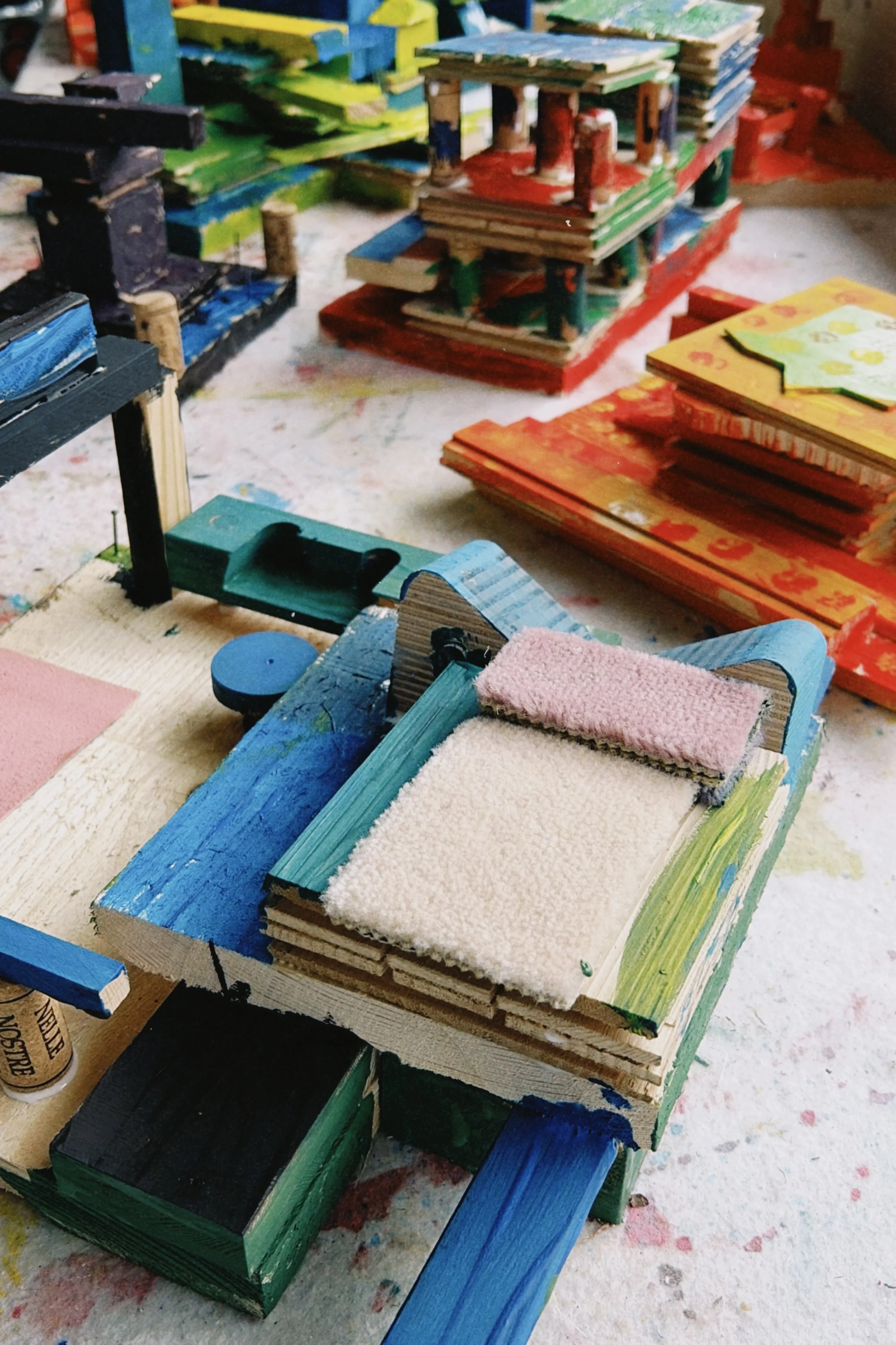 Bunte, handbemalte Holzstücke, die als Miniaturhäuser oder -gebäude auf einer Werkbank liegen.