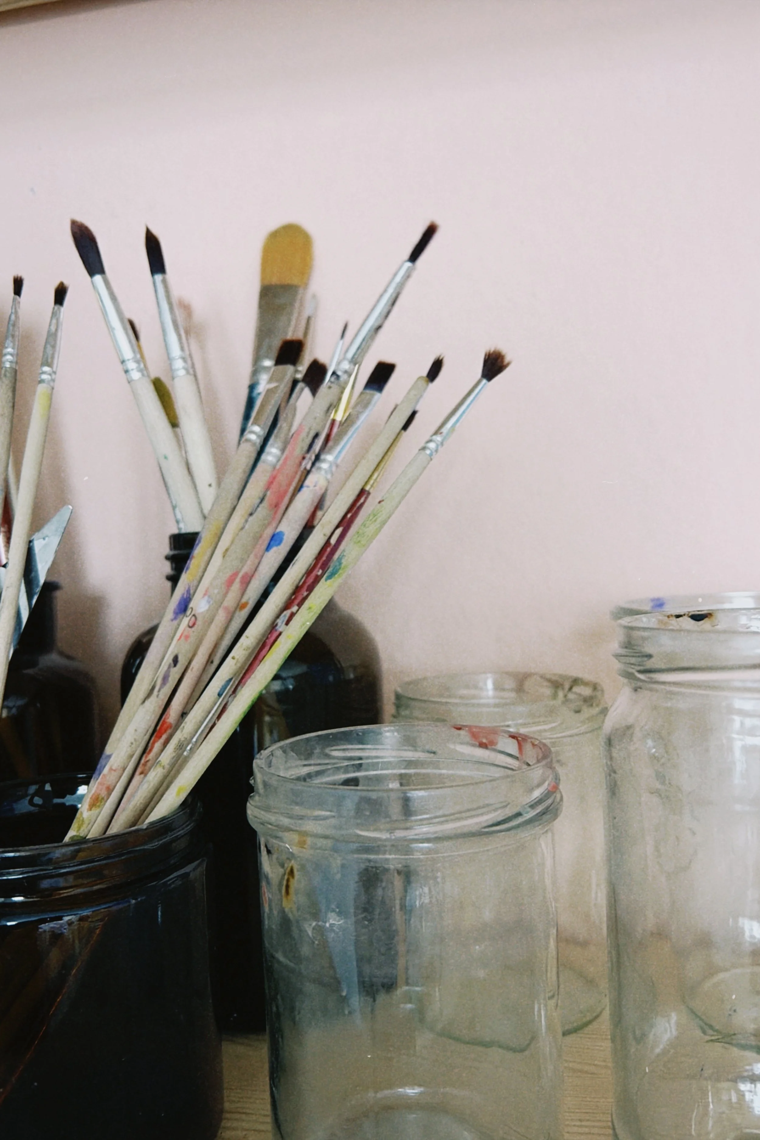 Verschiedene Pinsel in Gläsern, neben weiteren Gläsern und Malutensilien auf einem Tisch.