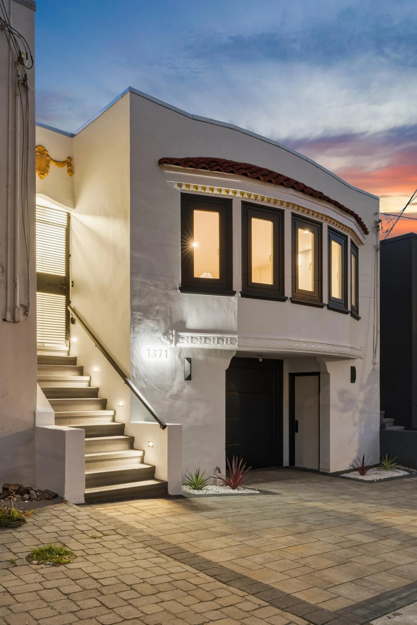 A modern two-story house with exterior stairs, black window frames, and architectural details at sunset.