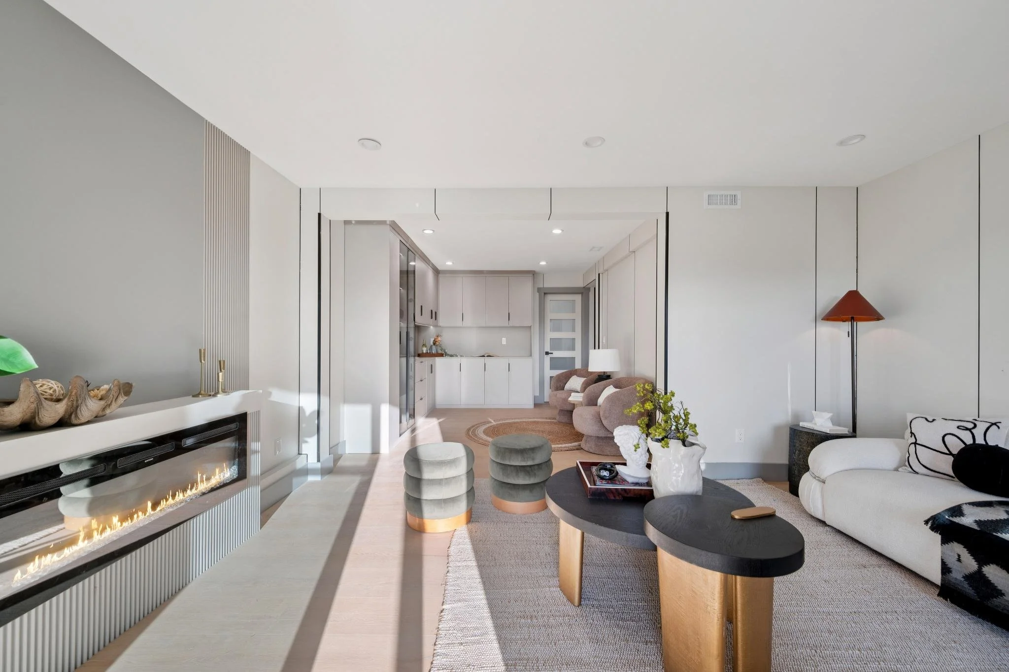 Modern living room with white walls, a fireplace, and neutral furniture including a white sofa and beige armchairs.