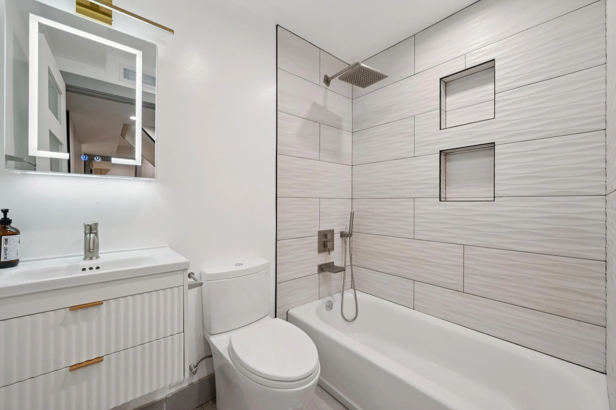 Modern bathroom with white vanity, toilet, and a bathtub with a rain showerhead and two built-in shelves in the shower wall