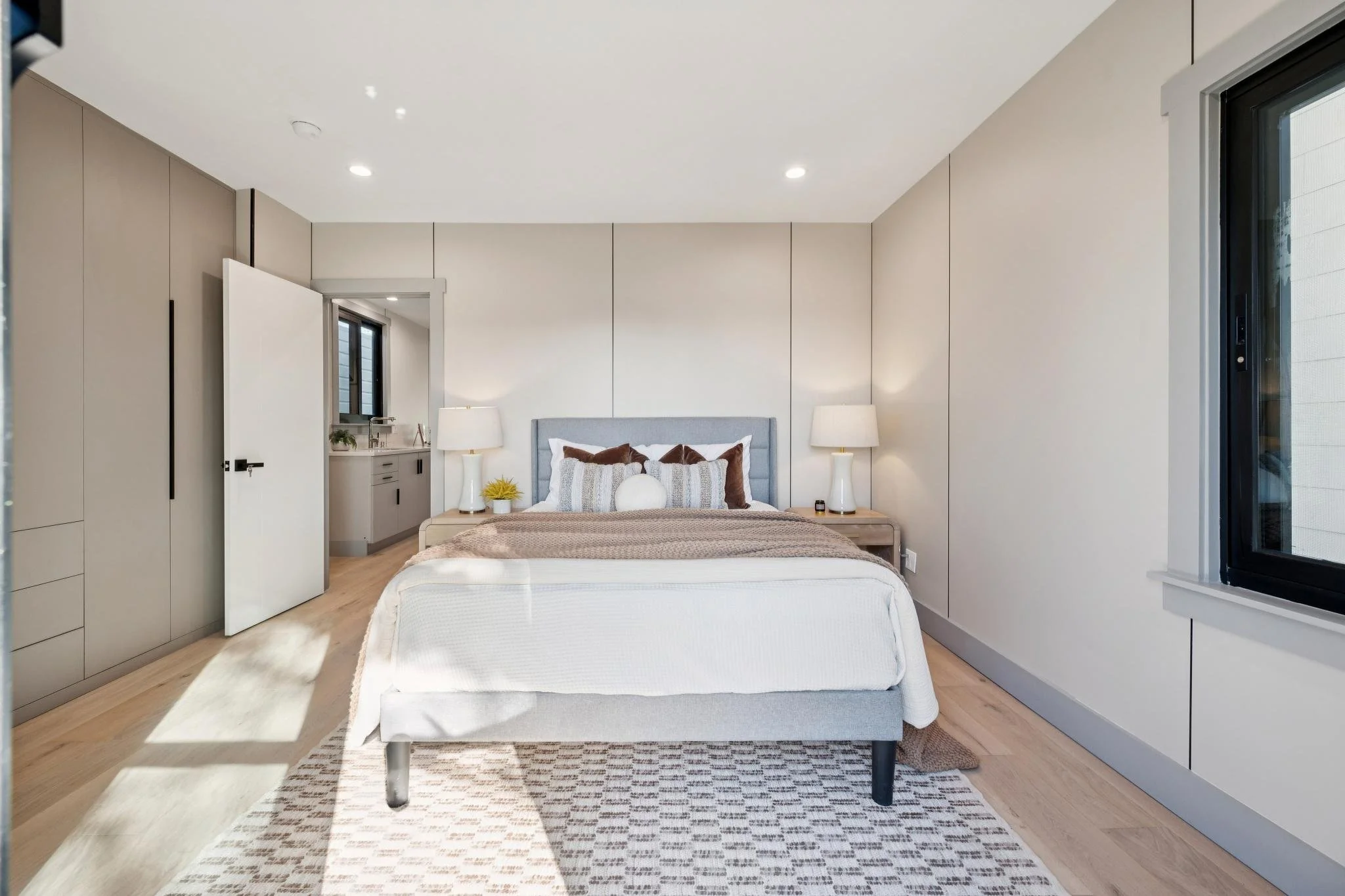 Modern bedroom with a bed, bedside tables with lamps, and a window with sunlight.