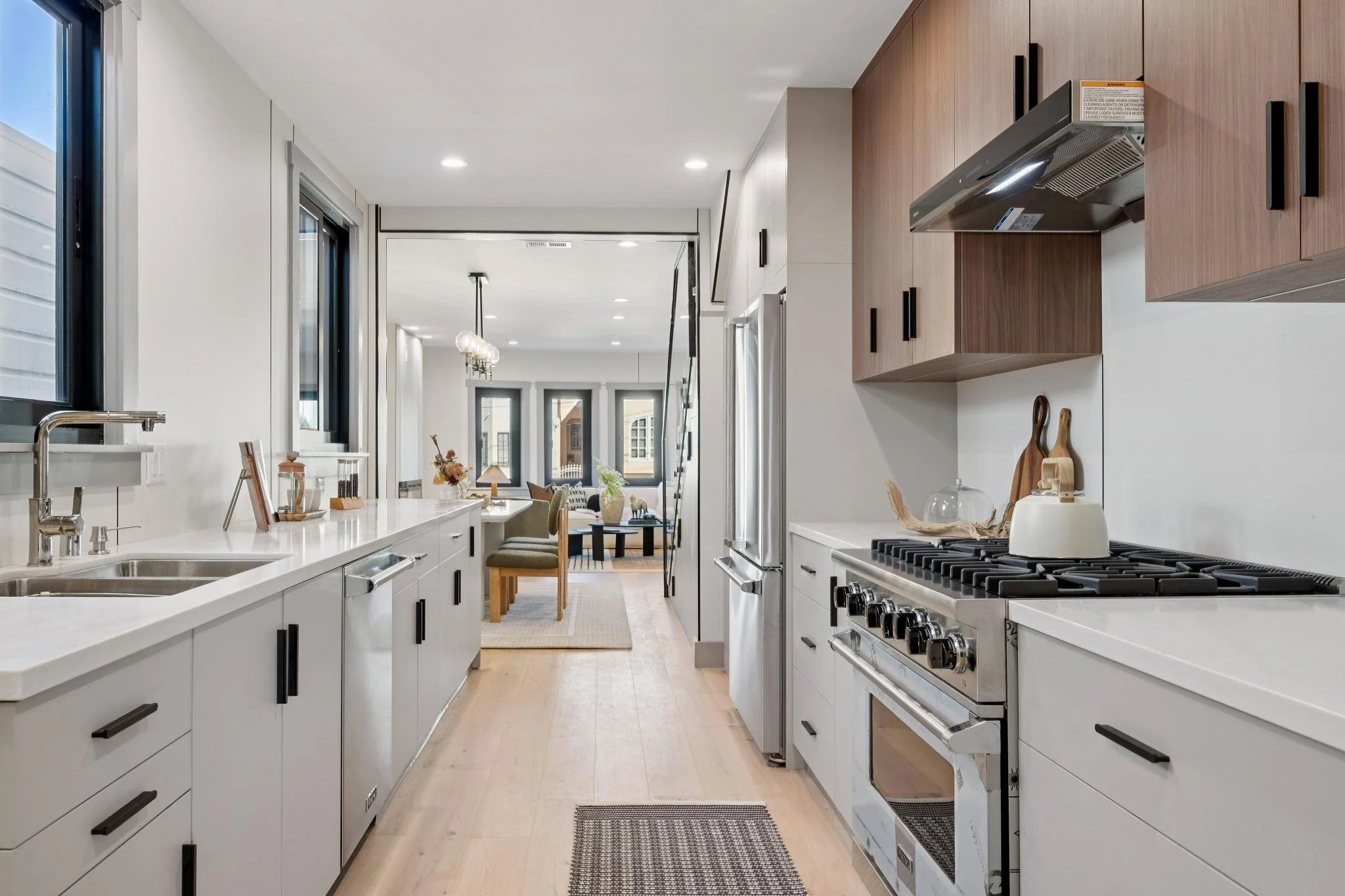 Modern kitchen with white cabinets, stainless steel appliances, and a view into the dining and living area with large windows.